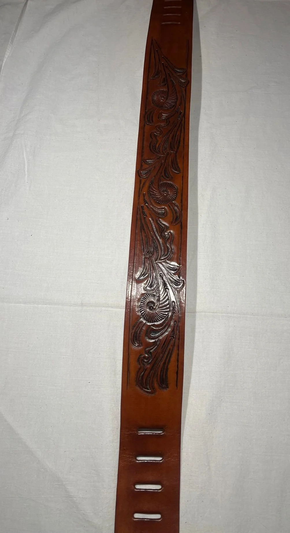 A wooden belt with carved decorative patterns of swirling shells and leaves.