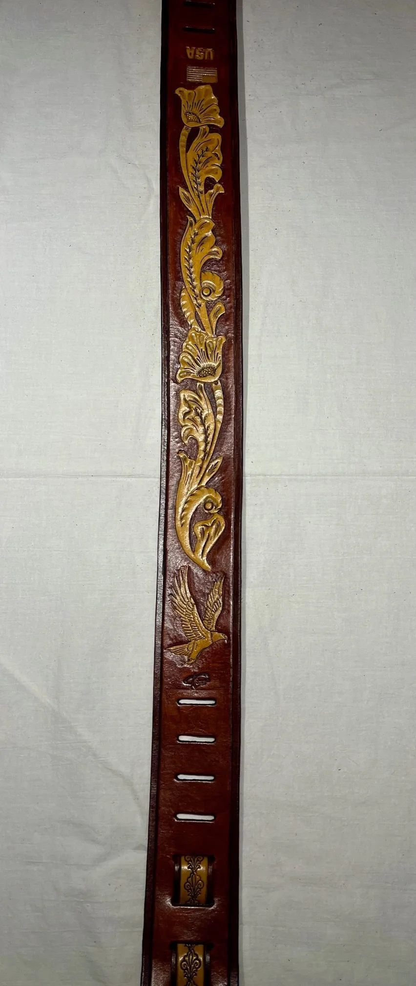 A decorative wooden belt with carved gold floral and bird patterns, and a belt buckle at the bottom.