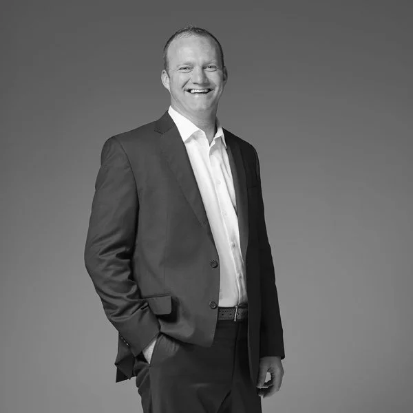 Black and white photo of a smiling man in a suit with hands in pockets.
