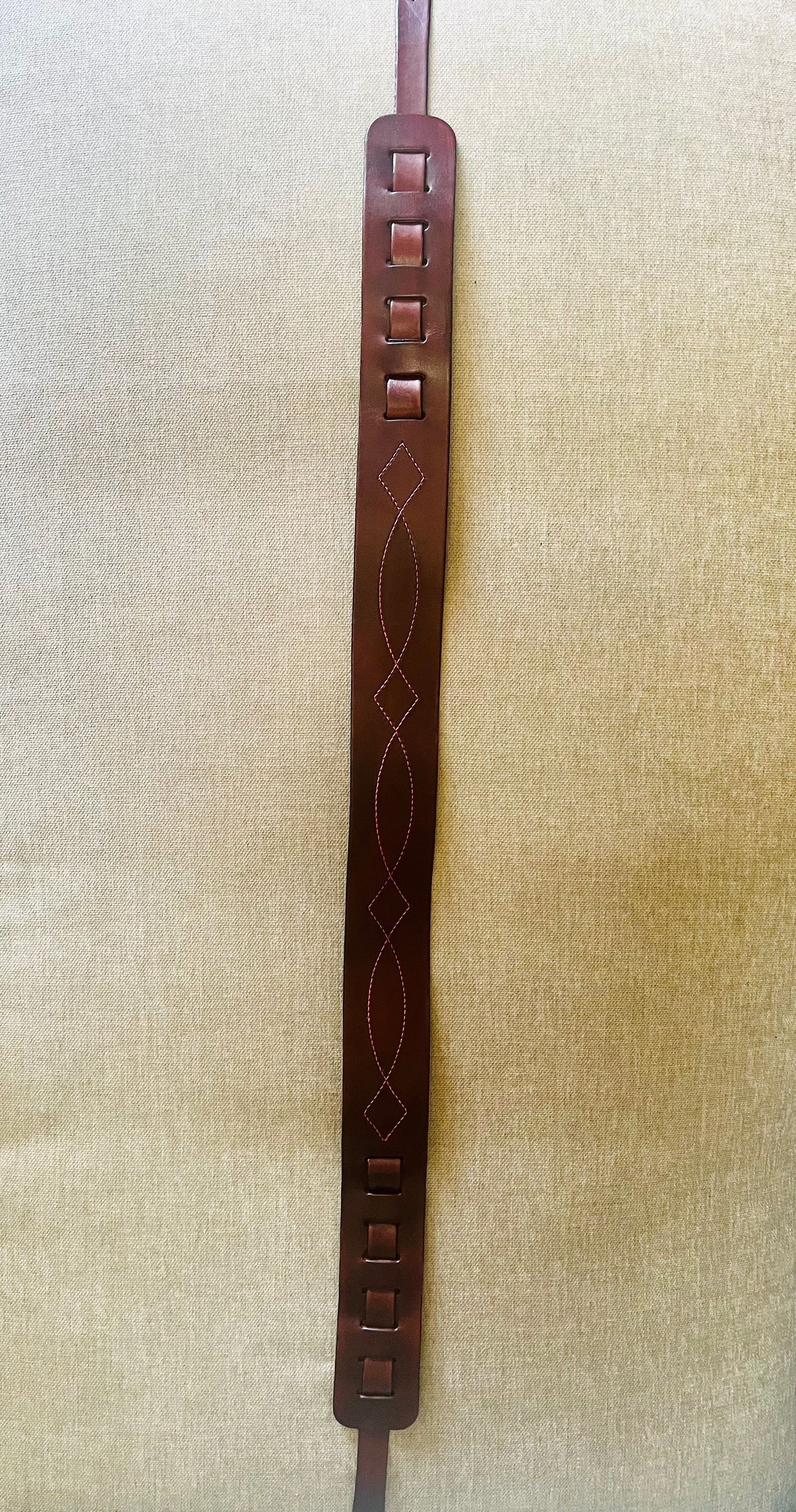 Brown leather bracelet with stitched pattern and square holes, hanging against a beige fabric background.