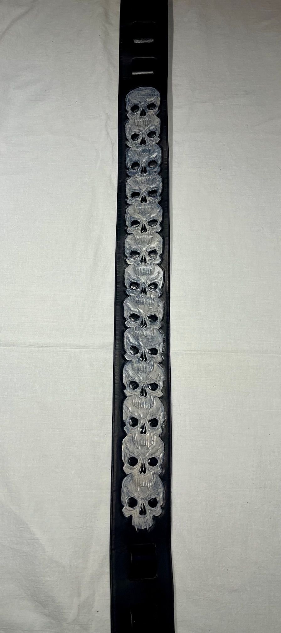 A black strap with multiple white skulls printed on it, laid flat on a light-colored surface.