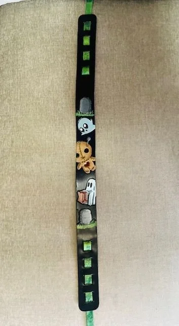 A black bracelet with cartoon ghost and creature characters, and green square accents.