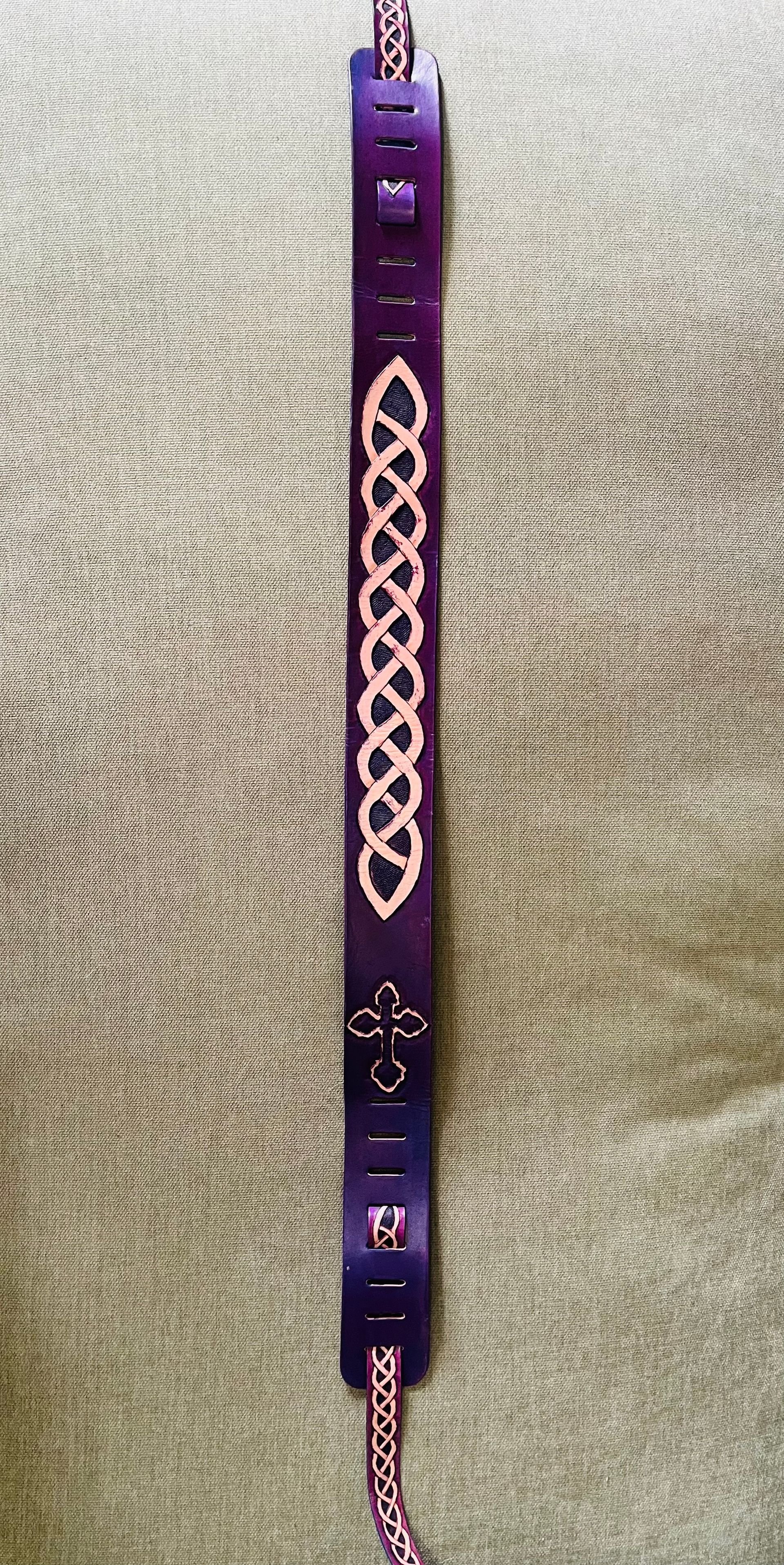A purple Celtic knot belt with a cross design and a pink and purple braided strap.