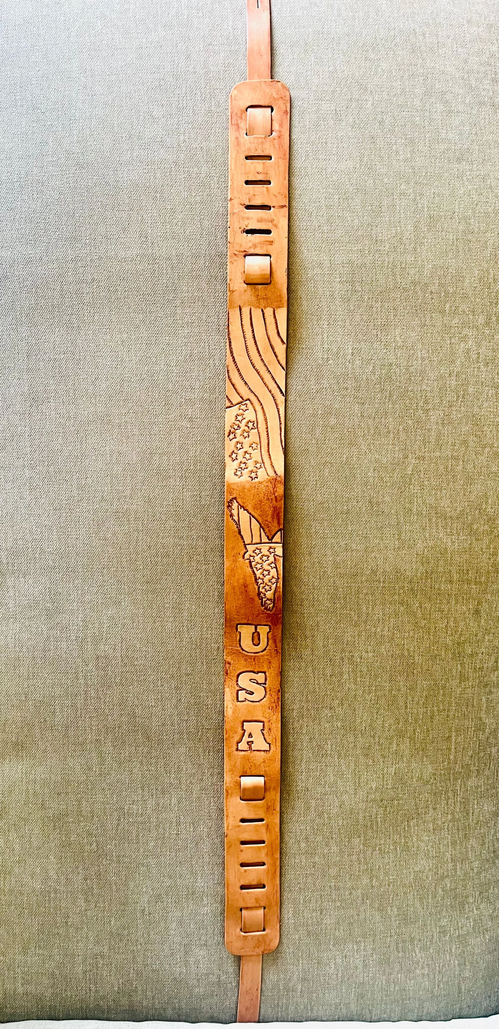 A wooden decorative piece with the cut-out words "USA" in the middle, situated vertically with a patterned section featuring stars and stripes, and a silhouette of the United States map above the word "USA."
