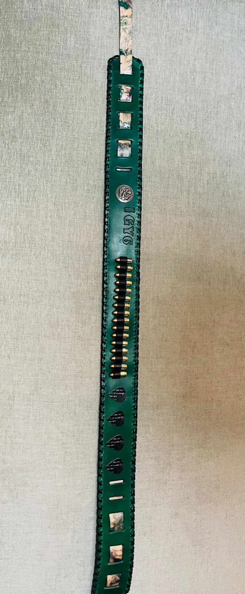 Close-up of a green belt with small holes and a row of black and gold bullet-shaped objects attached, laid against a gray surface.