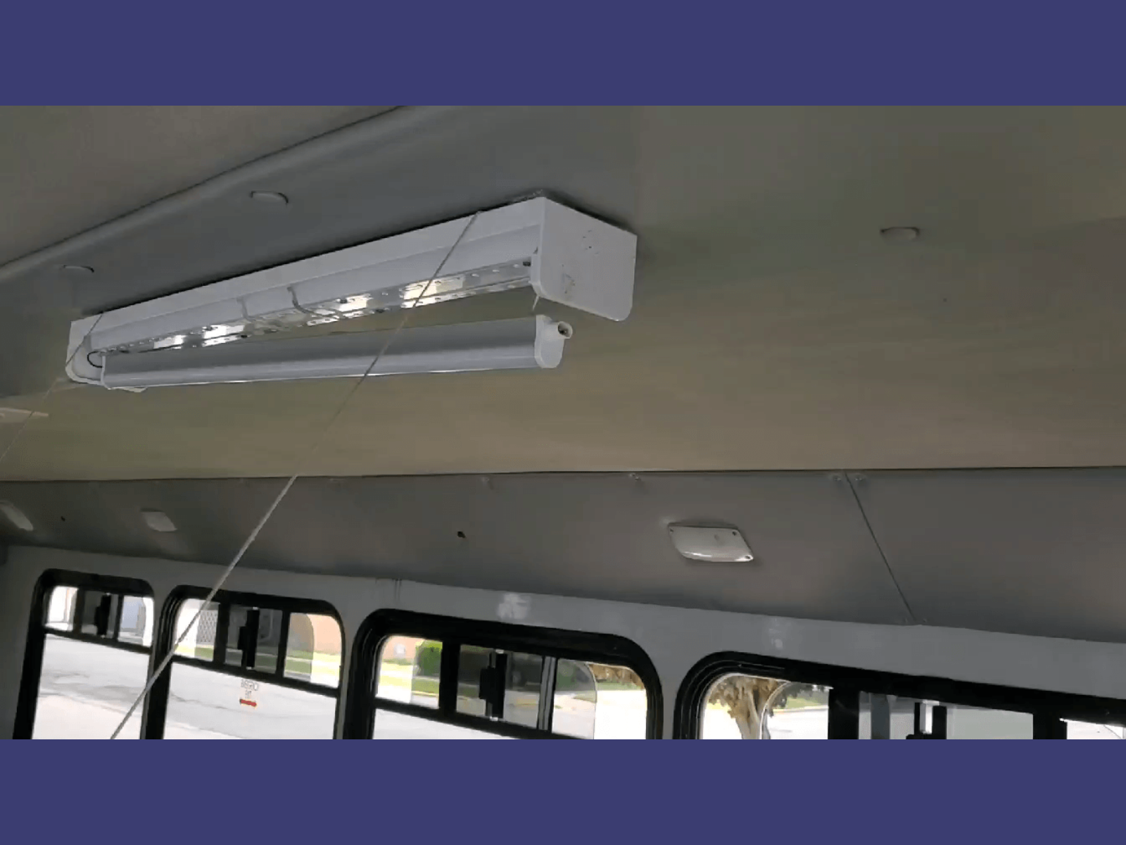 Interior of a bus showing a fluorescent light fixture, window with visible street outside, and ceiling panel.