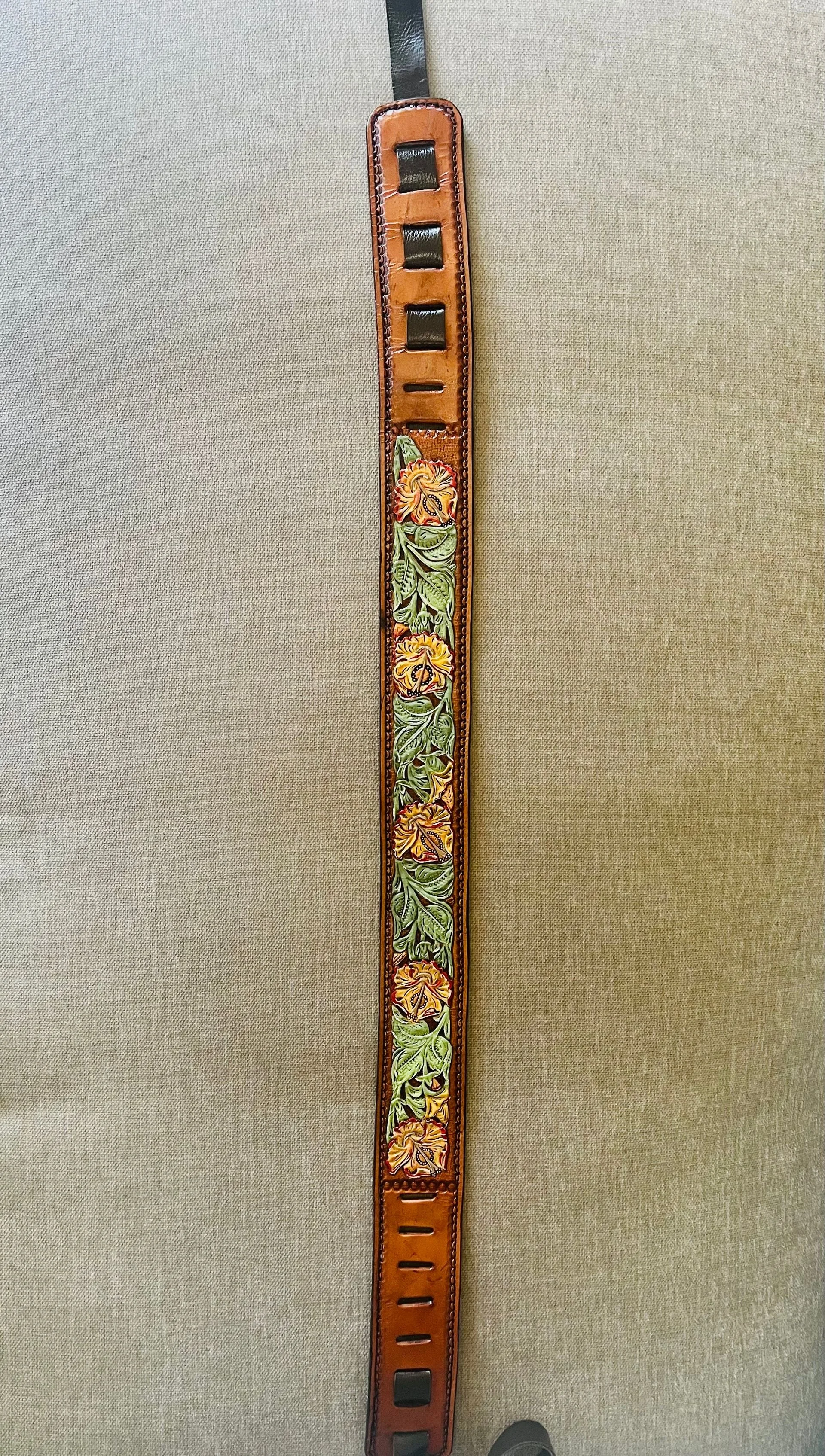 Leather belt with floral design, hanging vertically against a gray background.