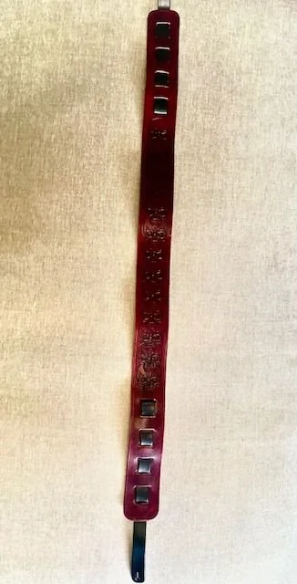 A red plastic LEGO piece with multiple rectangular holes and decorative embossed patterns, placed on a beige surface.