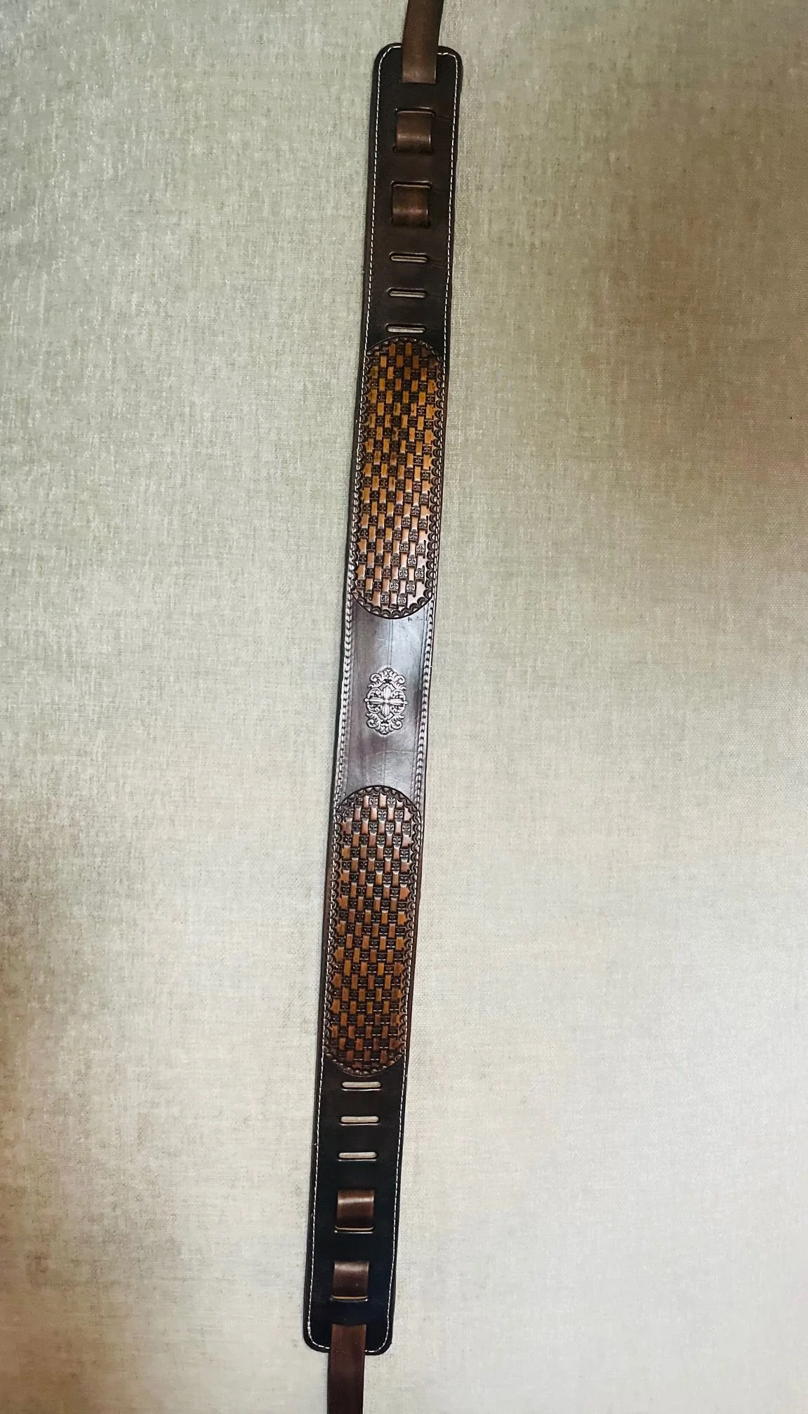 Western-style leather horse girth with decorative woven pattern and metal embellishments.