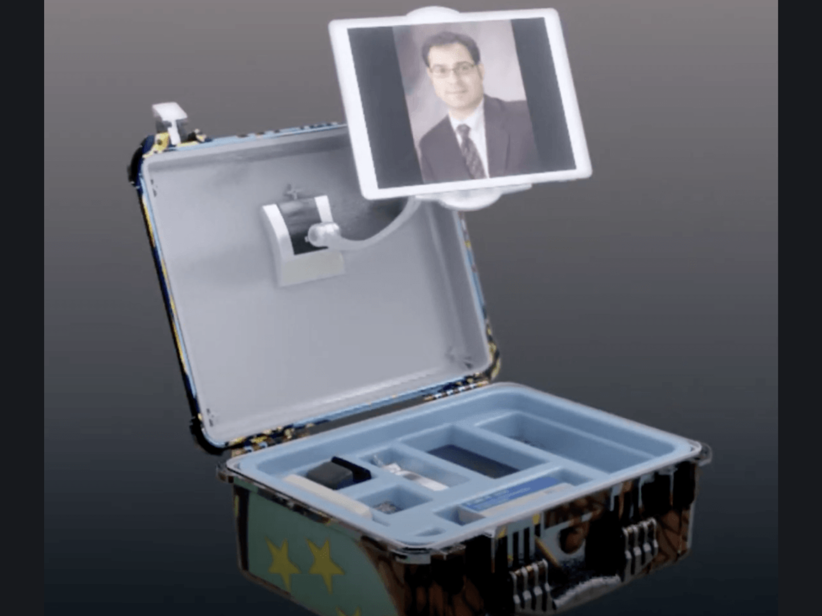 A metallic case with several compartments, and a detachable monitor displaying a person's face, possibly a robot or automated device.