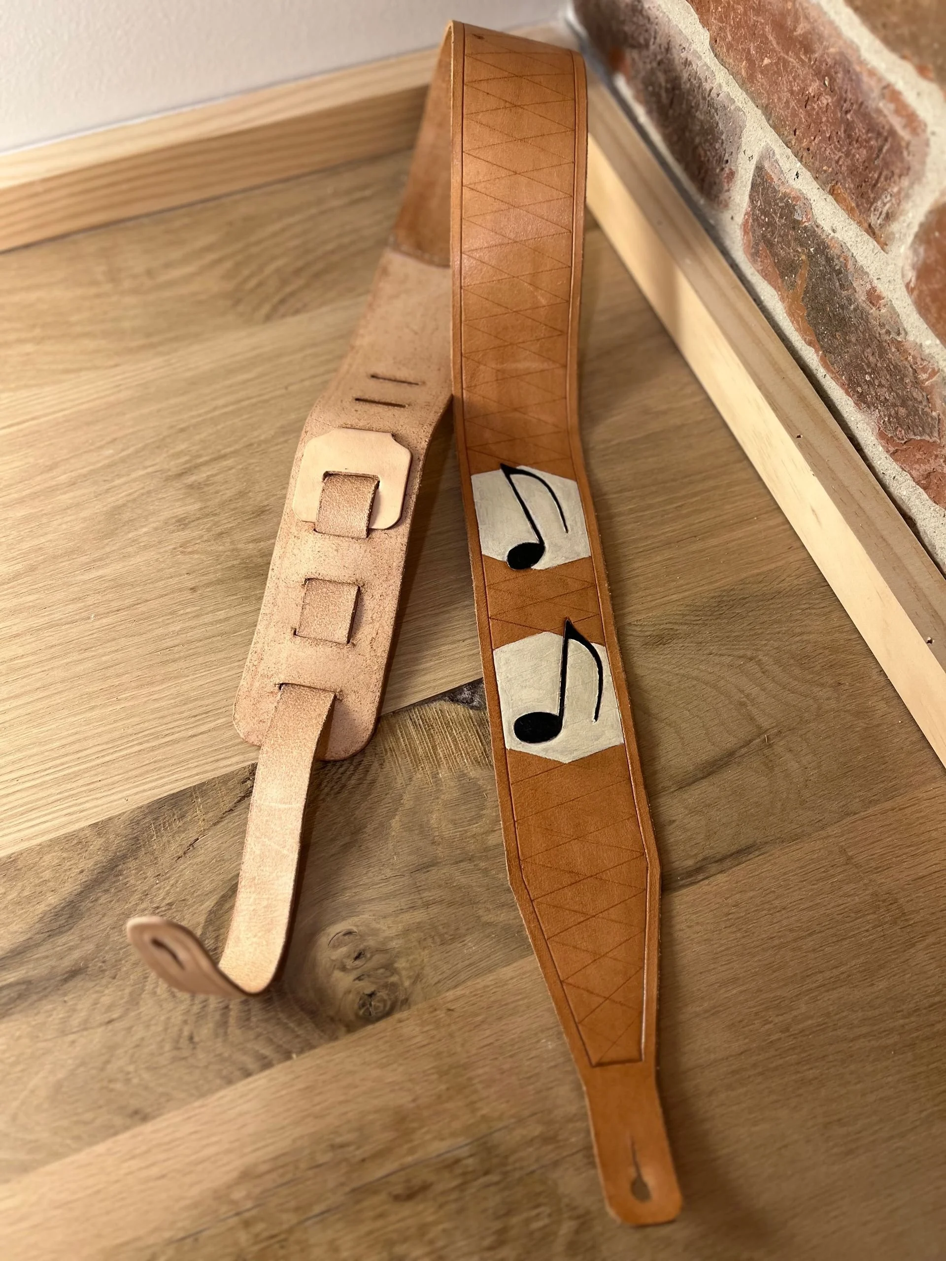 Two wooden bracelet-style bands, one with musical notes painted on it and the other with square cutouts, resting on a wooden floor next to a brick wall.