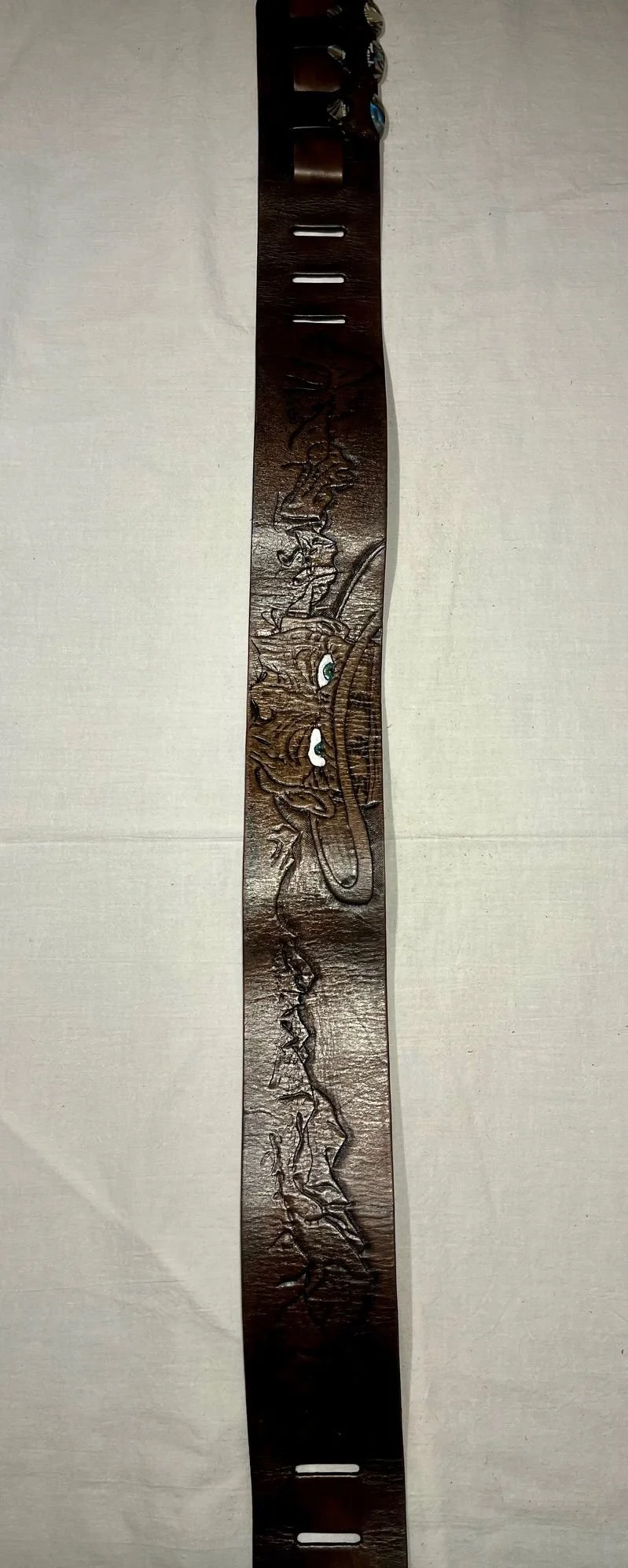 A carved wooden belt featuring a dragon design, laid flat on a light-colored surface.