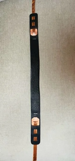 A black metal strap with copper-colored connectors on each end hanging vertically against a neutral background.