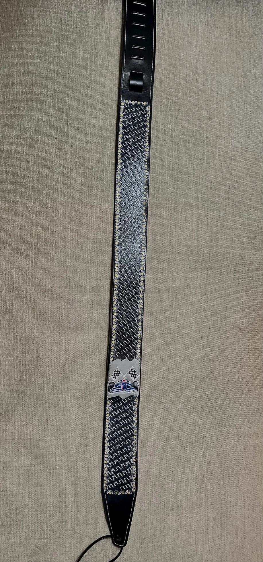 A black lanyard with a decorative pattern and a small badge or logo featuring a racing car and checkered flags.
