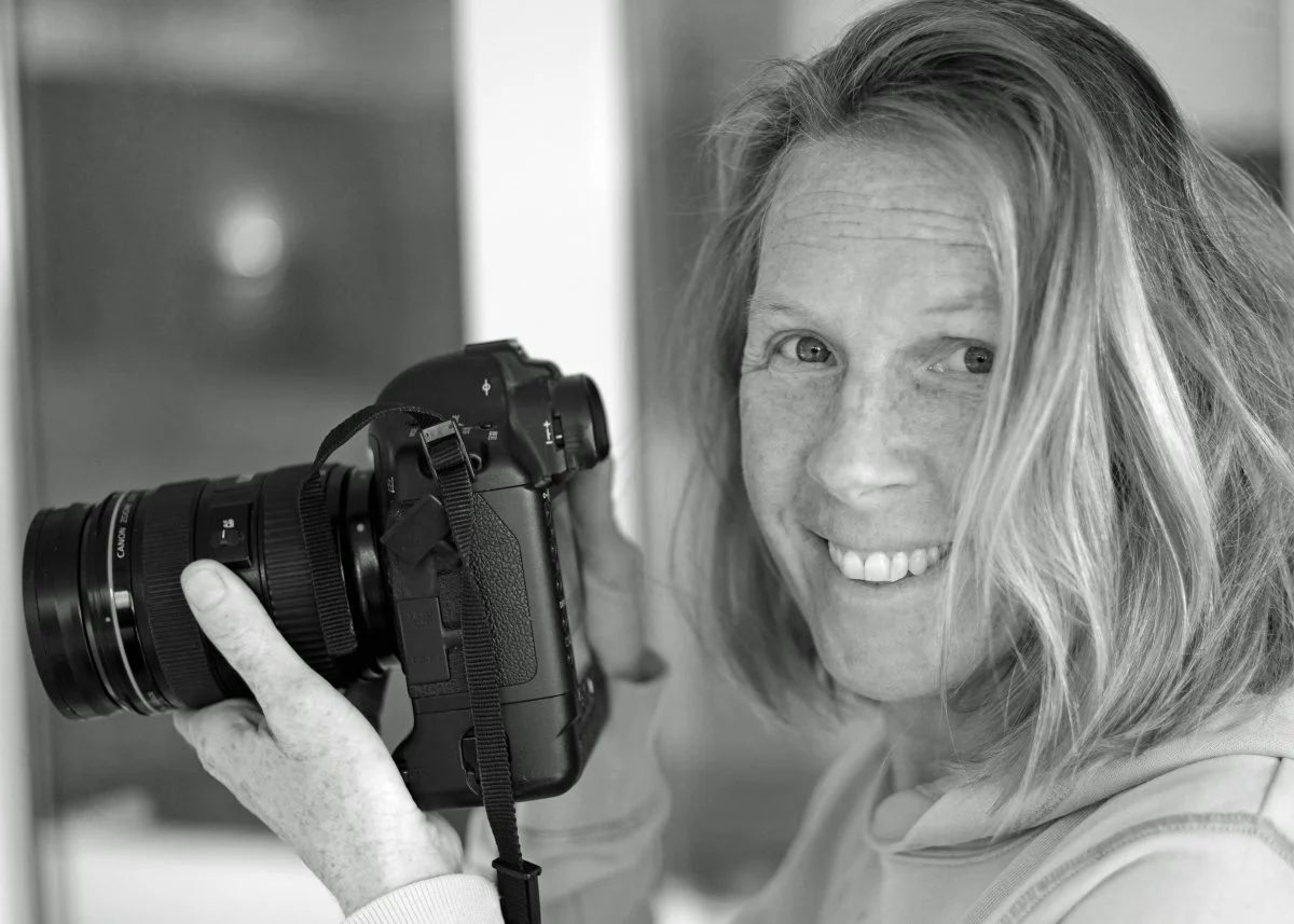 A smiling woman with shoulder-length hair holding a camera and looking at the camera.