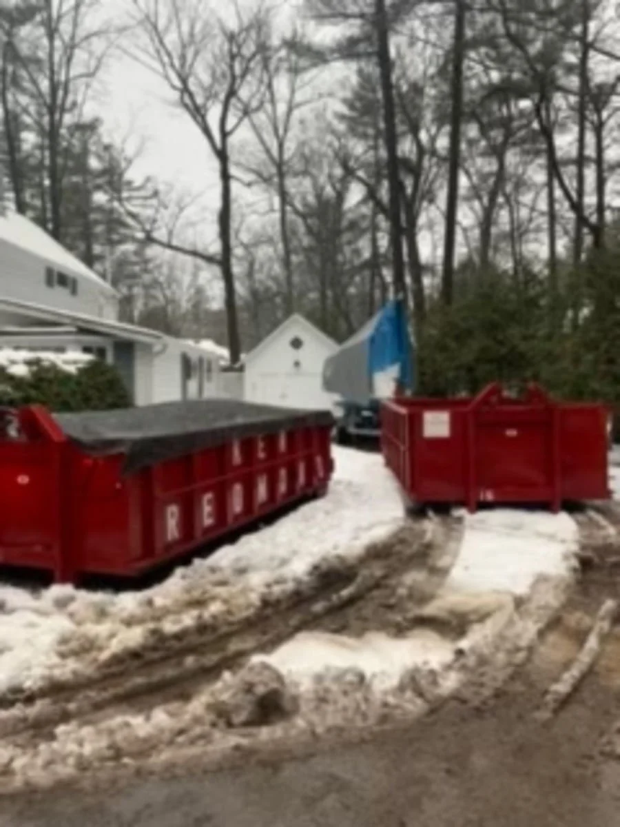 Red garbage dumpsters labeled "REPUBLIC" on a snowy residential street with tire tracks and tall leafless trees in the background.