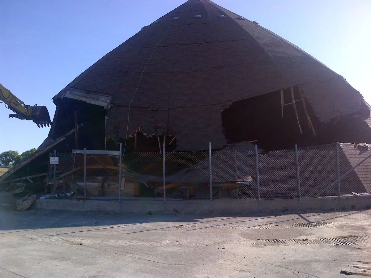 Destroyed building with a damaged roof behind a chain-link fence.