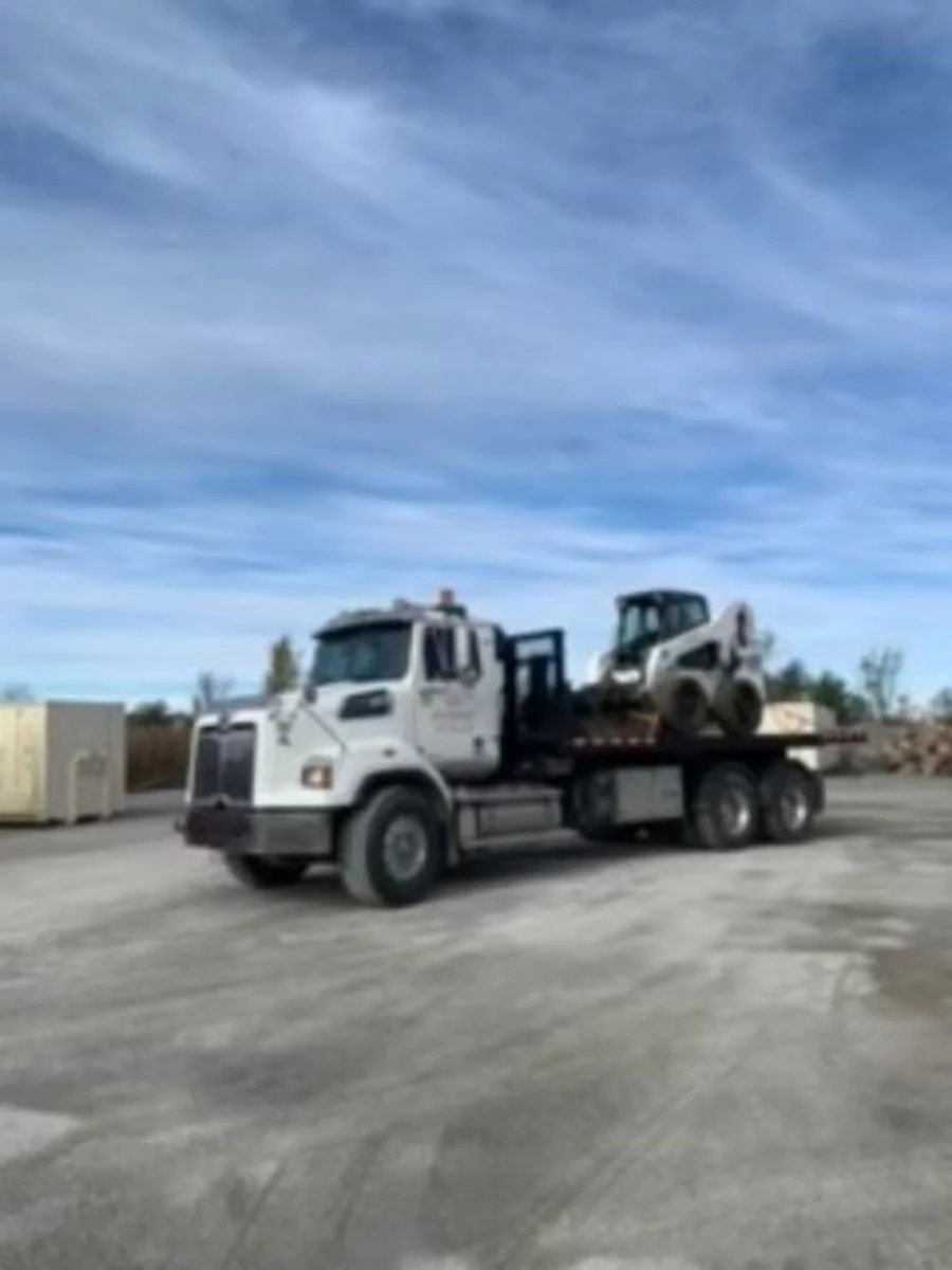 A flatbed tow truck carrying a skid steer loader