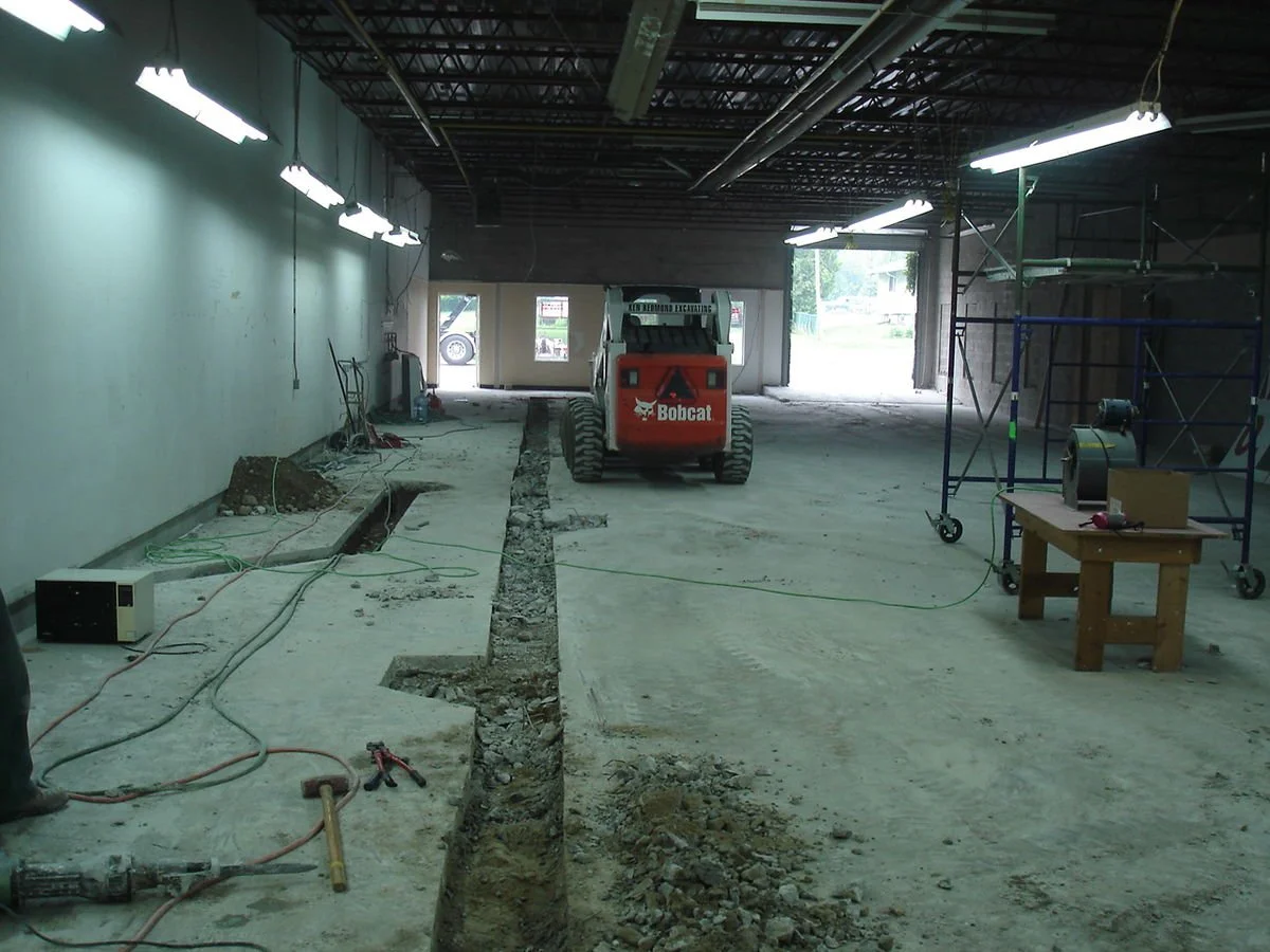 Interior of a construction site with a Bobcat skid-steer loader, scaffolding, and building materials, indicating ongoing renovation or construction work.