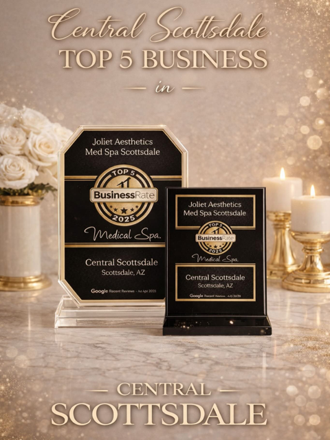 Recognition plaques for Central Scottsdale's top 5 business in 2023 awarded to Joliet Aesthetics Med Spa Scottsdale with gold and black accents placed on a marble surface, surrounded by candles and white flowers.