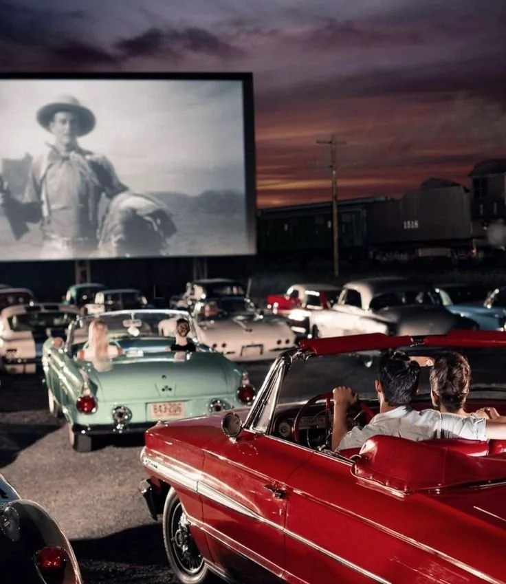 Une projection d'un film sur écran géant dans un cinéma en plein air, entourée par des voitures anciennes  garées, avec un coucher de soleil en arrière-plan. Un événement immersif qui fait voyager dans le temps.