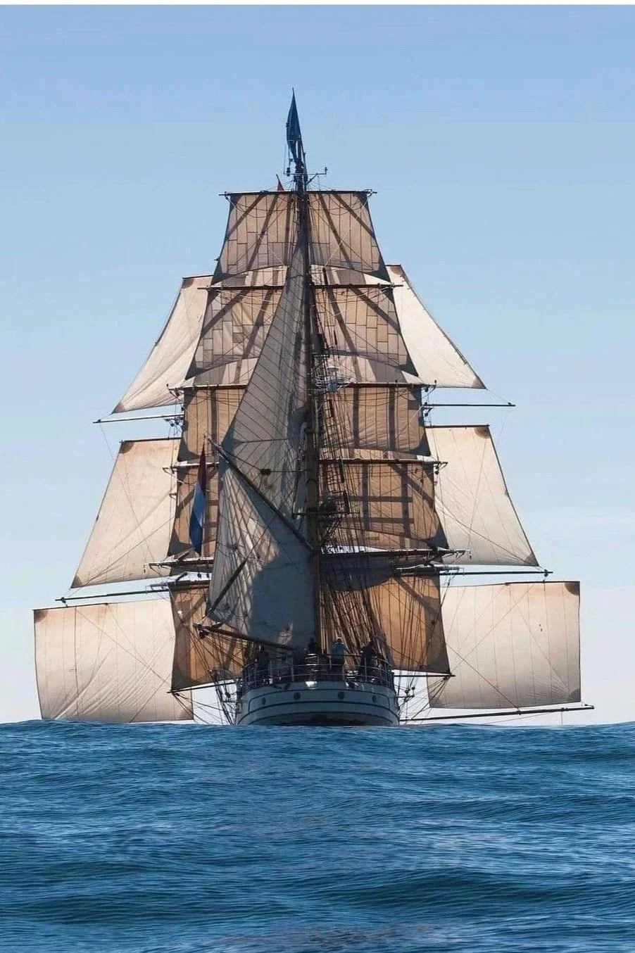 Un grand voilier ancien naviguant sur la mer avec ses voiles déployées contre un ciel clair.