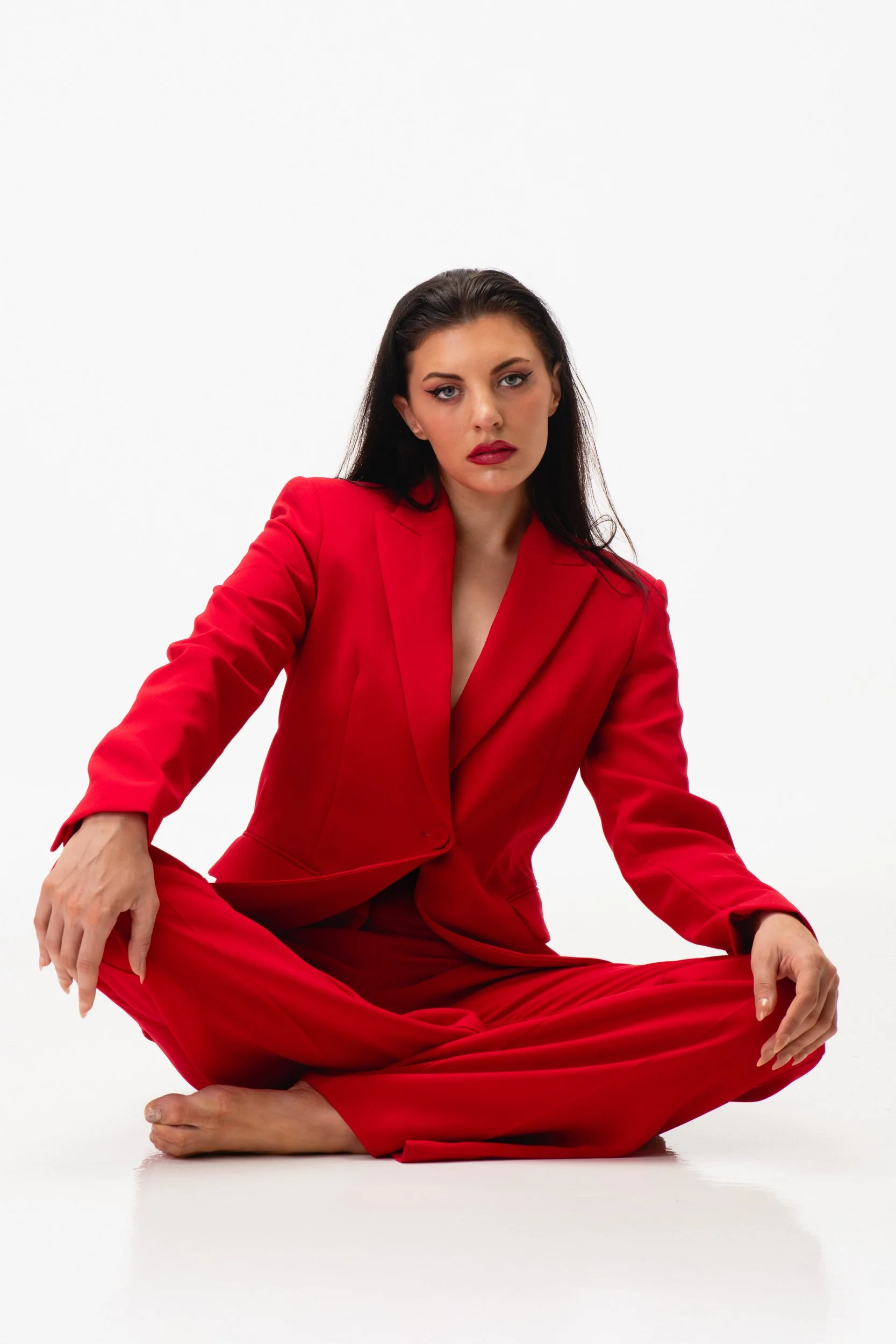 Woman in a red pantsuit sitting cross-legged on the floor against a plain white background.