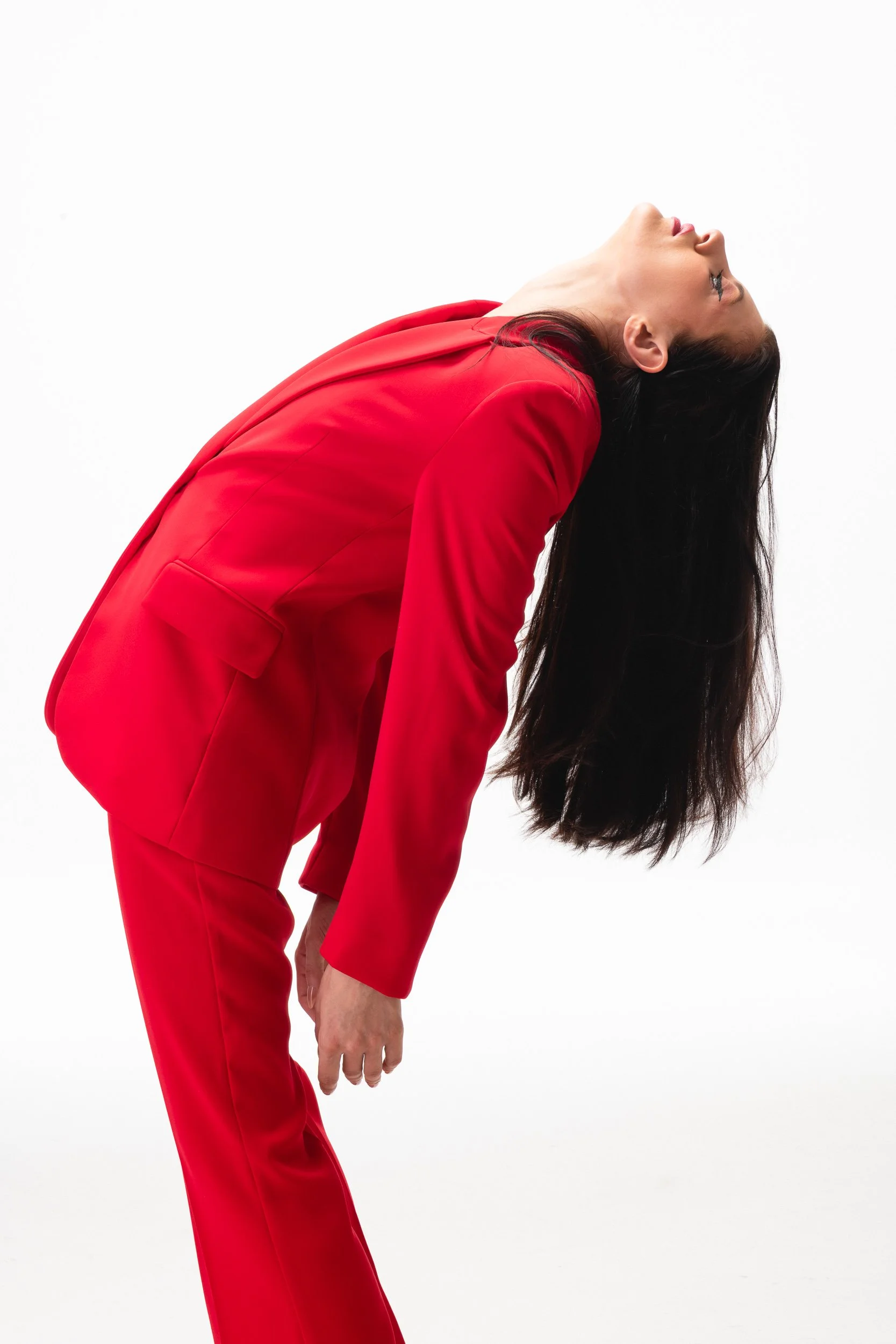 Woman in a red suit bending backward with her head thrown back and hair hanging down.
