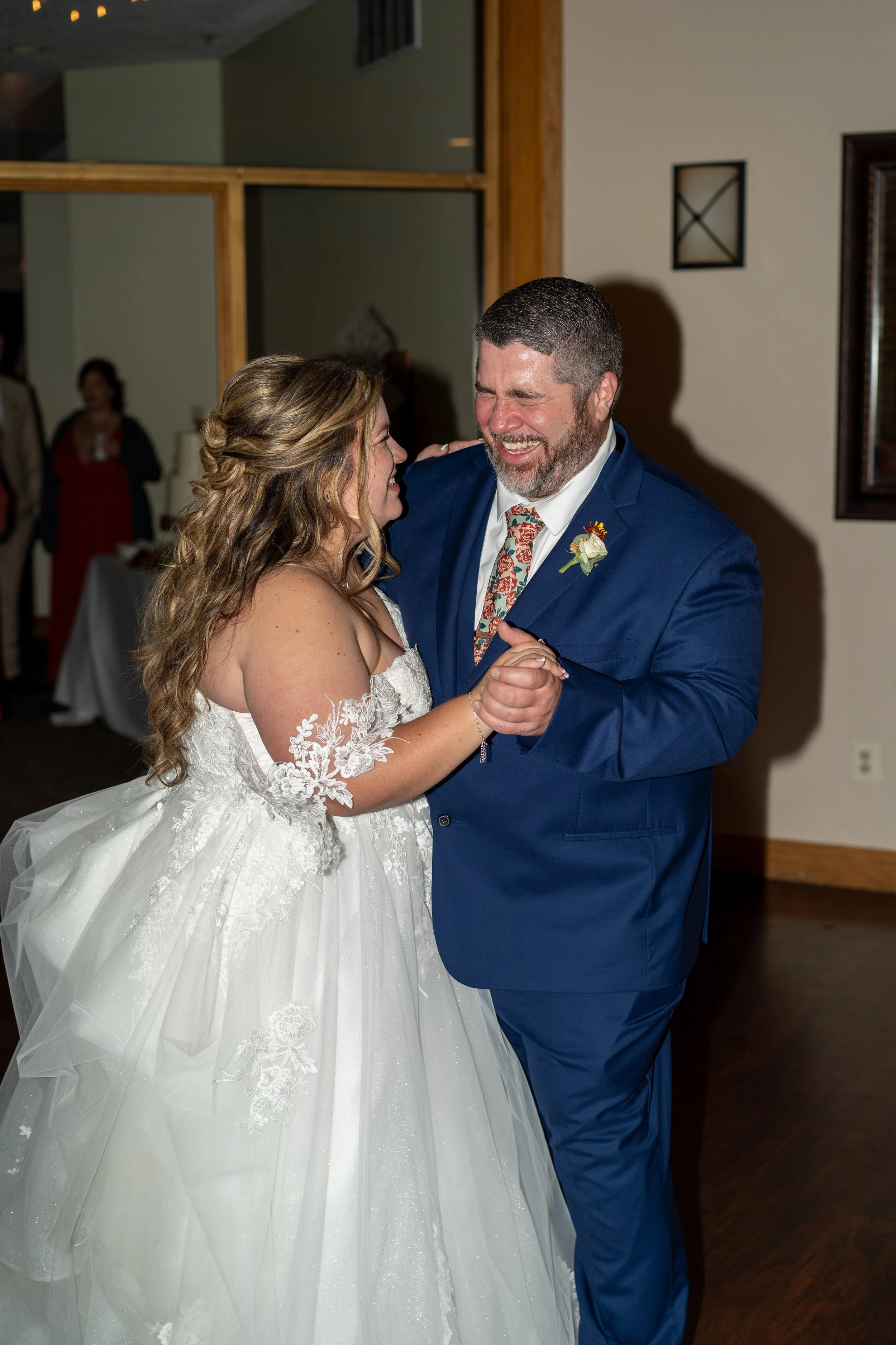 A bride in a white wedding dress dancing with a man in a blue suit at a wedding reception.