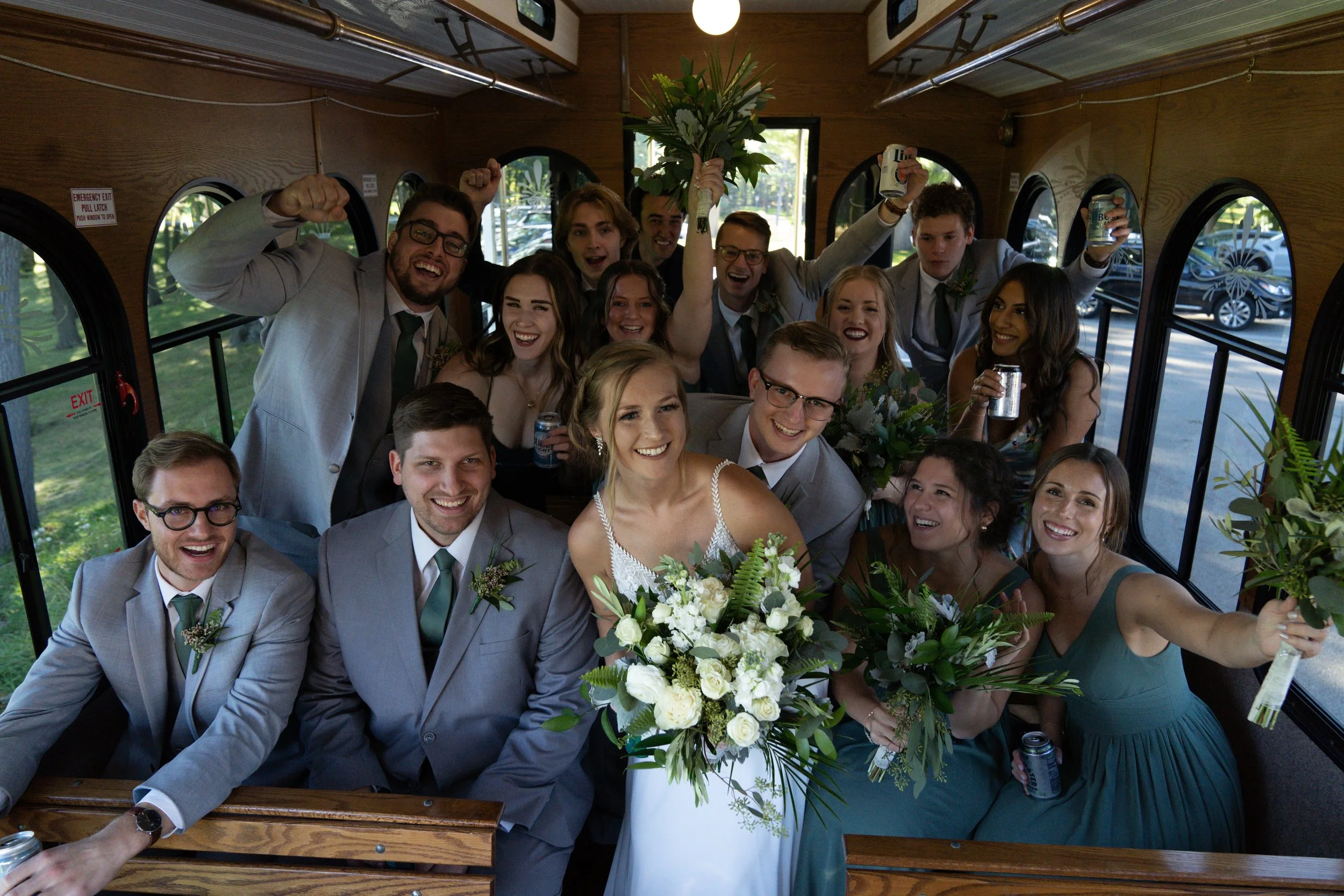 A wedding celebration inside a bus with the bride and groom at the center, surrounded by joyful friends and family holding bouquets and drinks, with a lot of smiles and excitement.