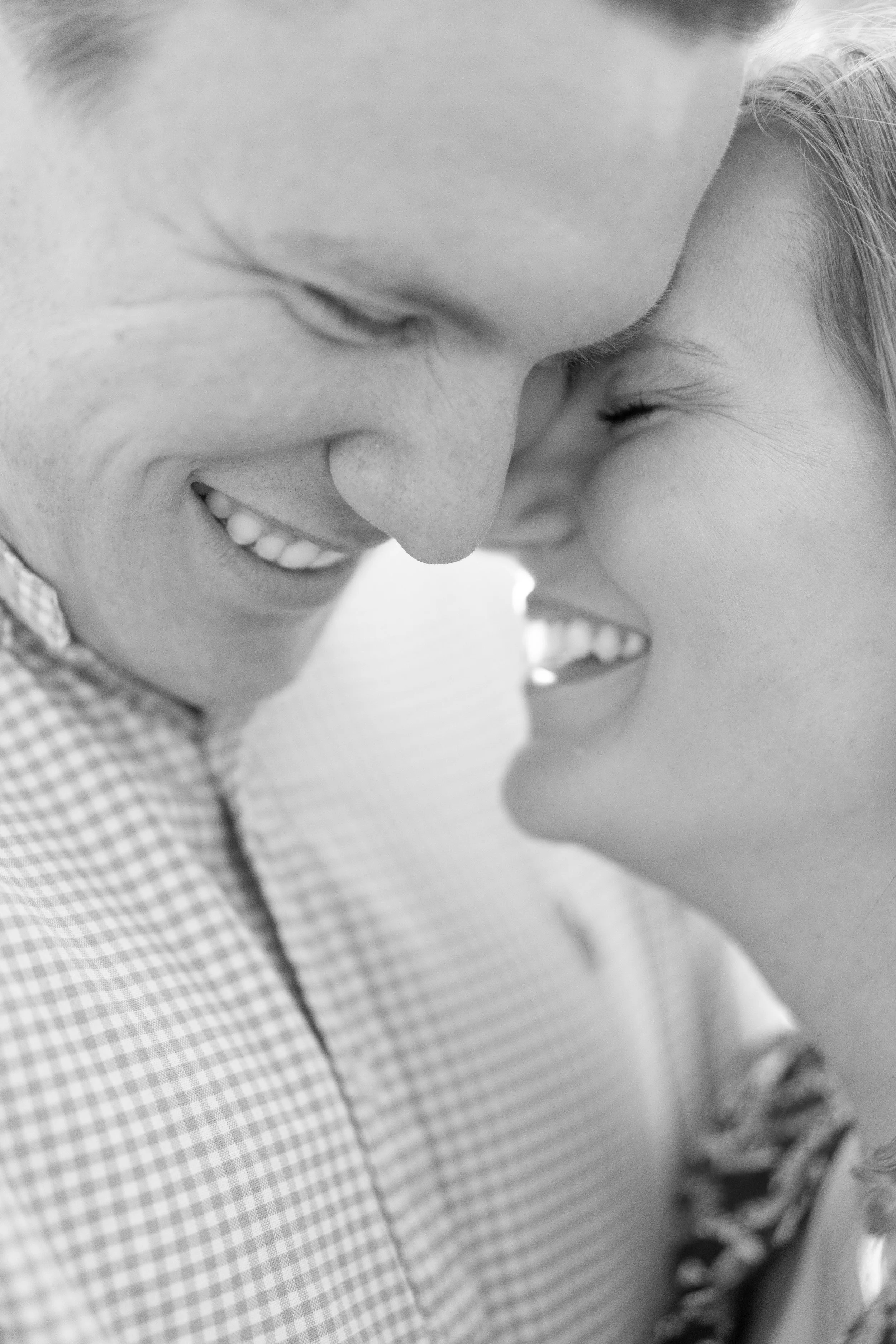 A close-up black and white photo of a couple smiling and touching foreheads.