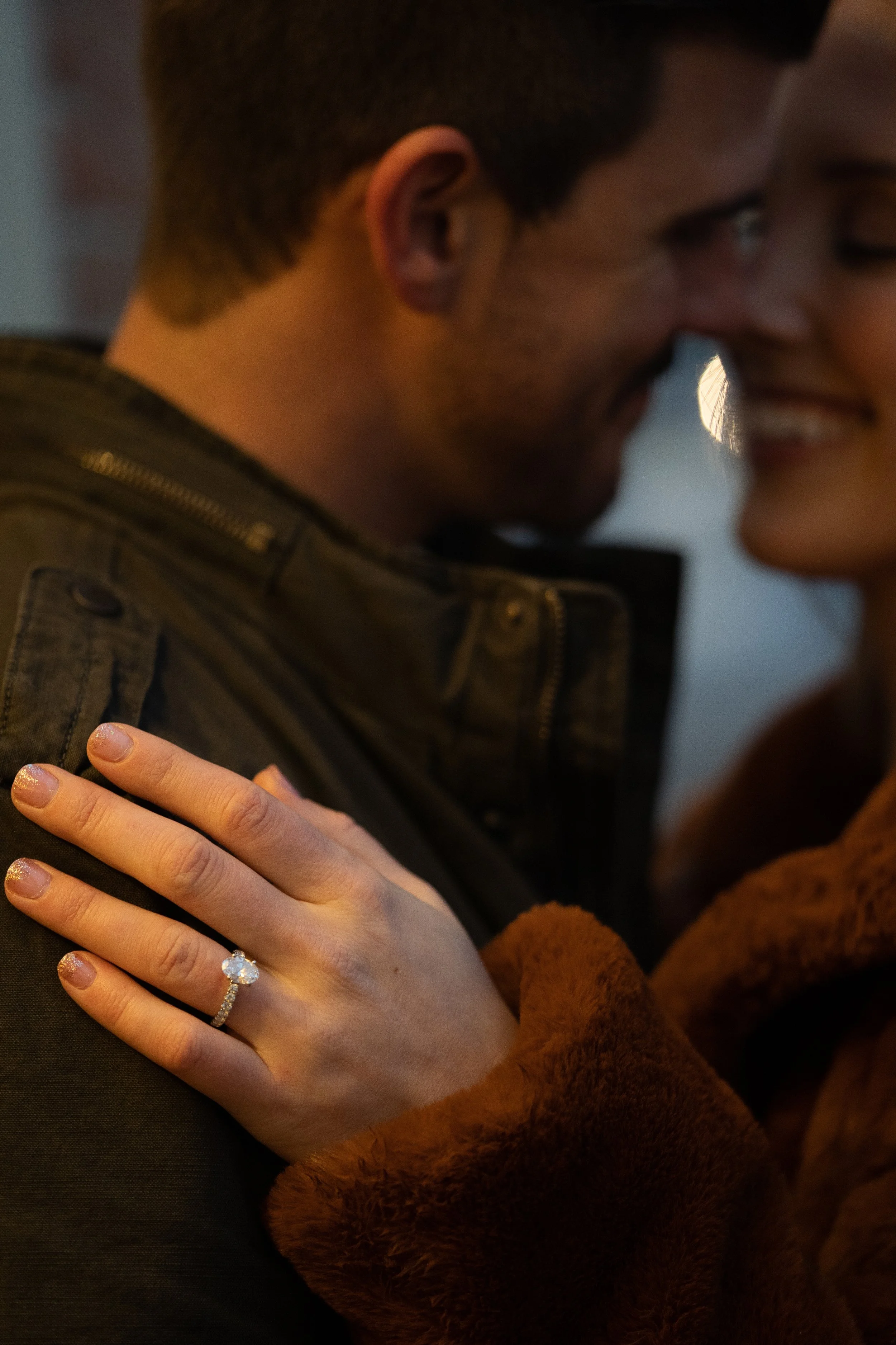Close-up of a happy couple embracing, with the woman showing an engagement ring on her finger.