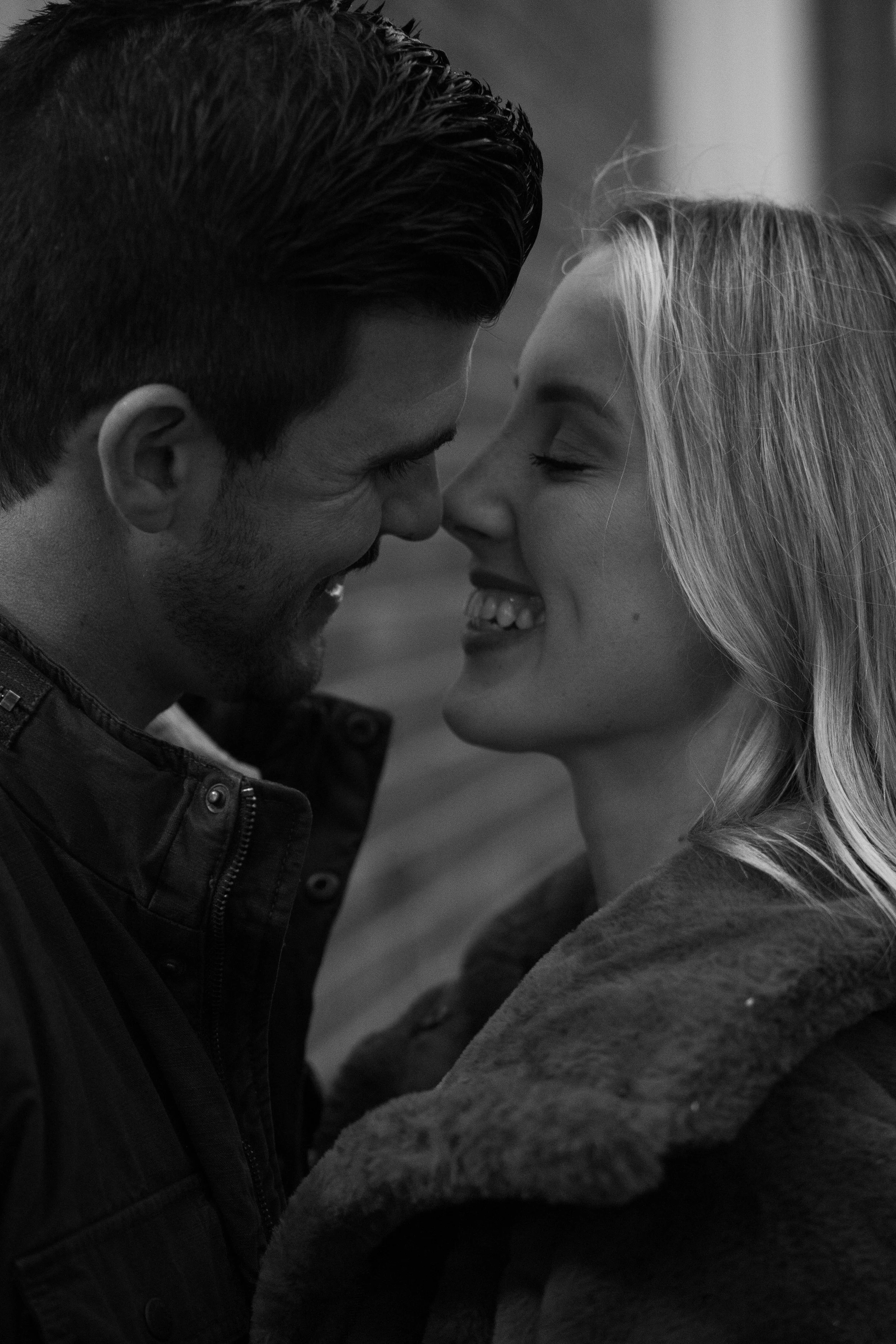 A black and white close-up of a couple smiling and touching foreheads, showing affection.
