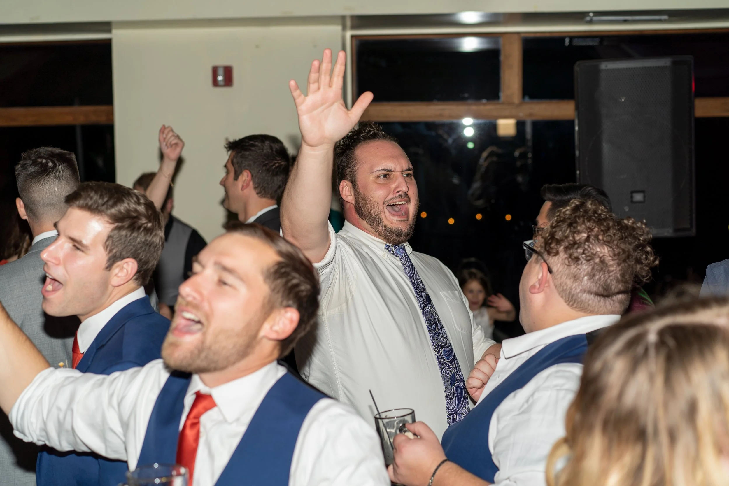 People celebrating at a lively event, some dancing and raising their hands, dressed in formal attire.