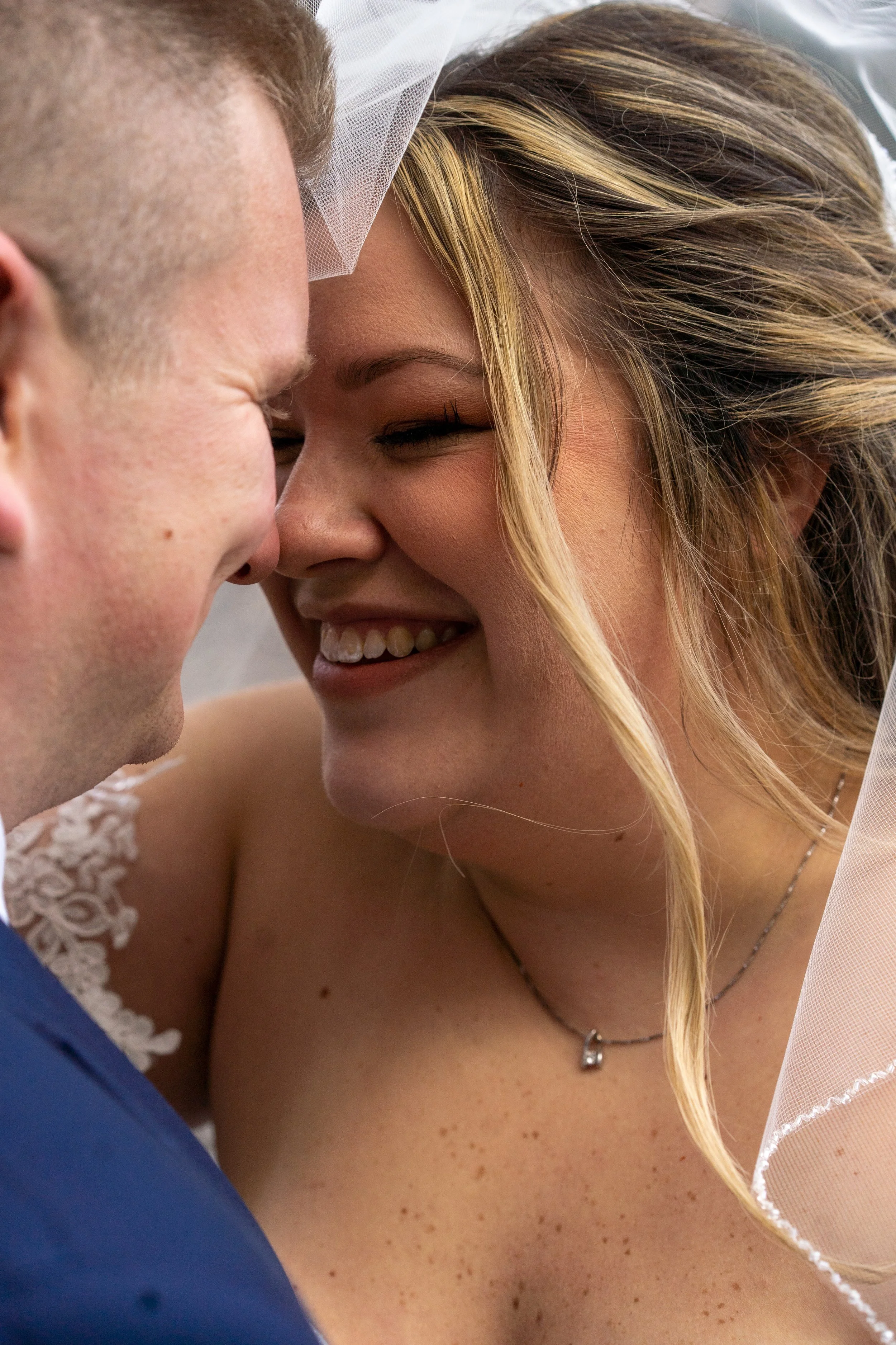 Close-up of a joyful bride and groom sharing a kiss at their wedding, smiling with faces close together.