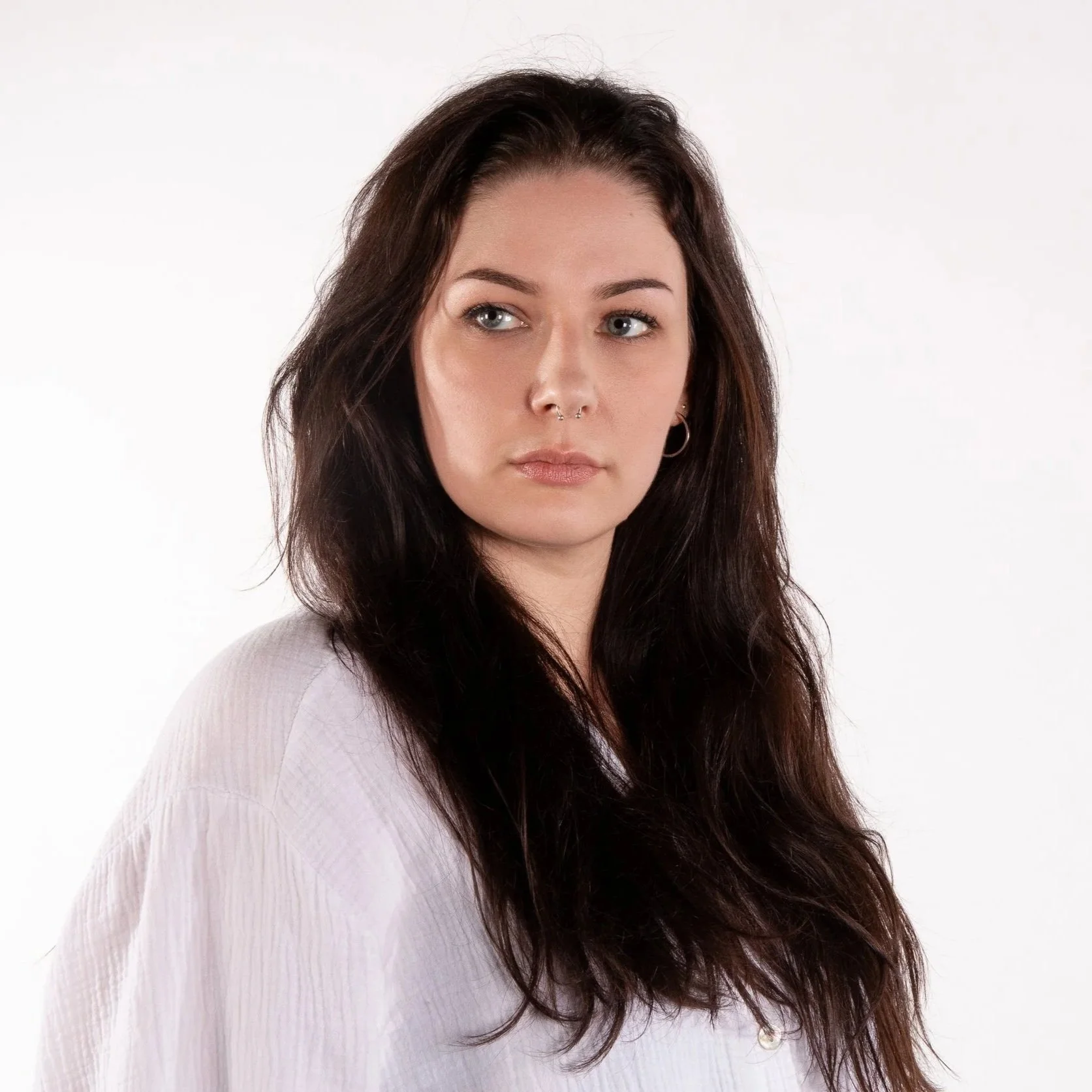 Portrait von Daria Berndt. Junge Frau mit dunklen Haaren und weißer Bluse vor einem weißen Hintergrund.
