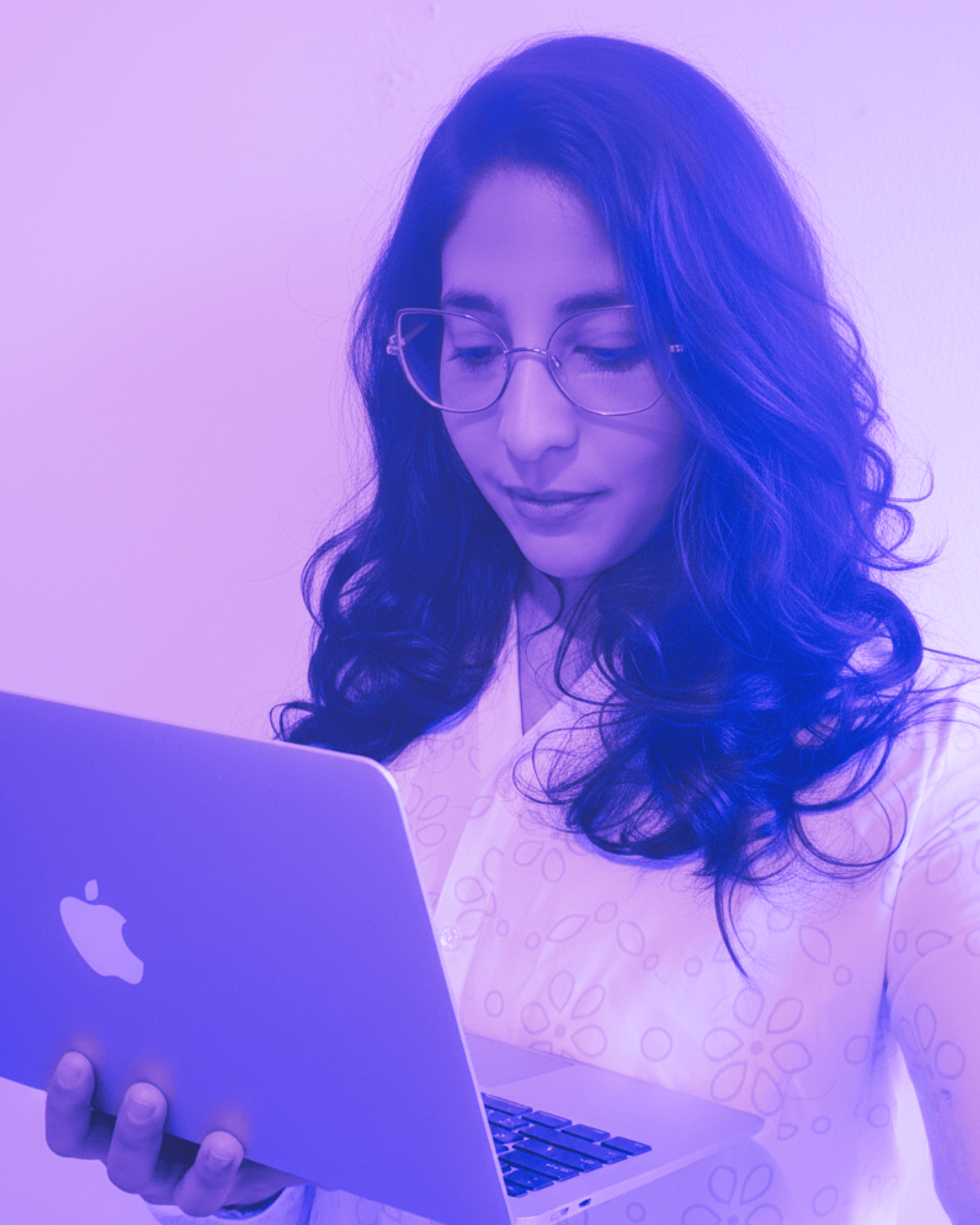Mujer con gafas mirando una laptop Apple.
