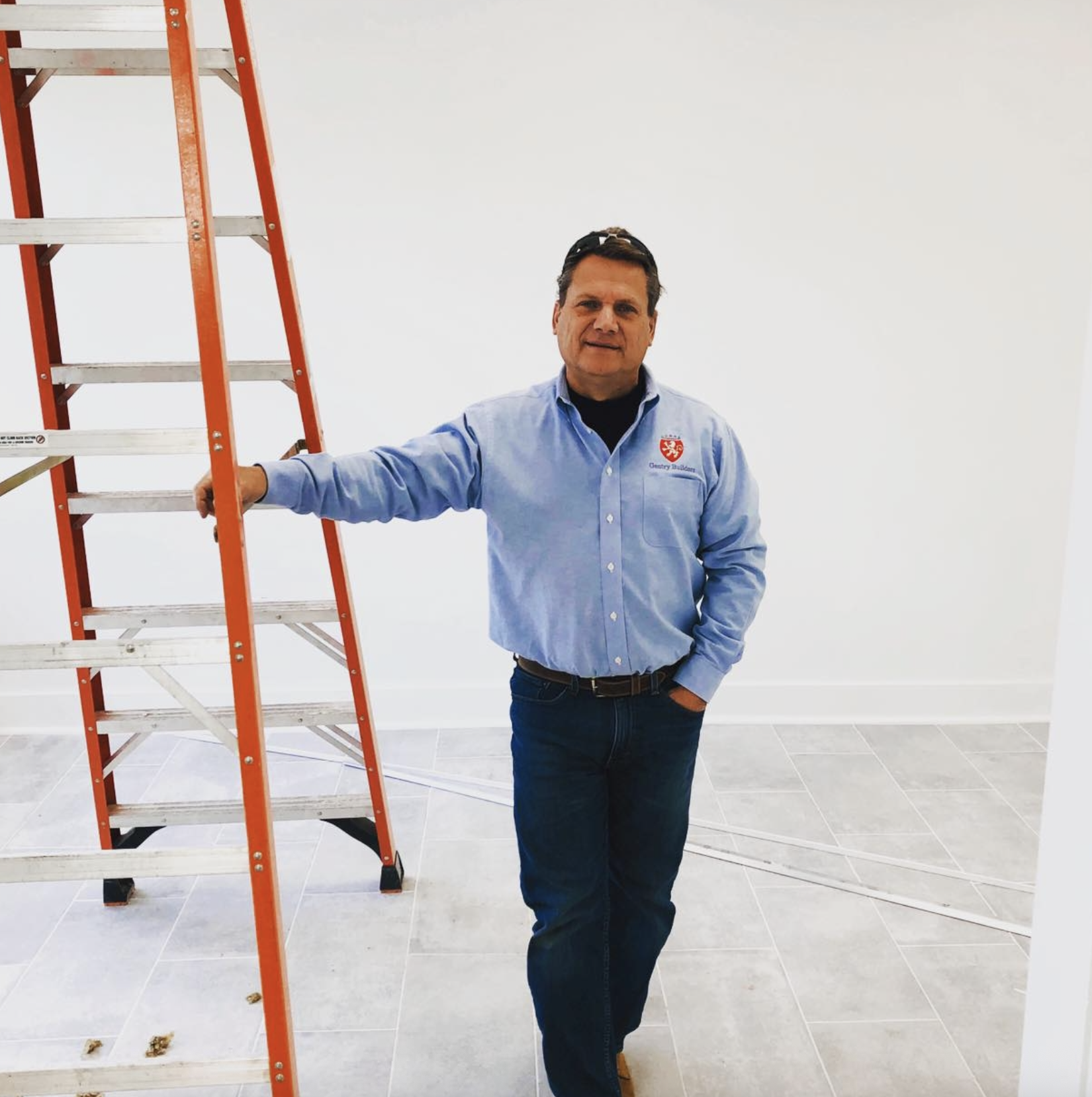 Man standing next to an orange ladder in an indoor setting with white walls and tiled floor