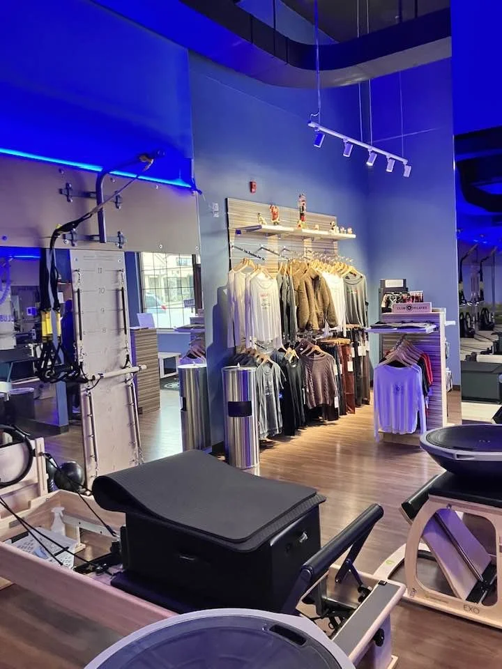 Indoor gym with workout equipment and clothing display, featuring workout machines, rack of clothes, and modern lighting.