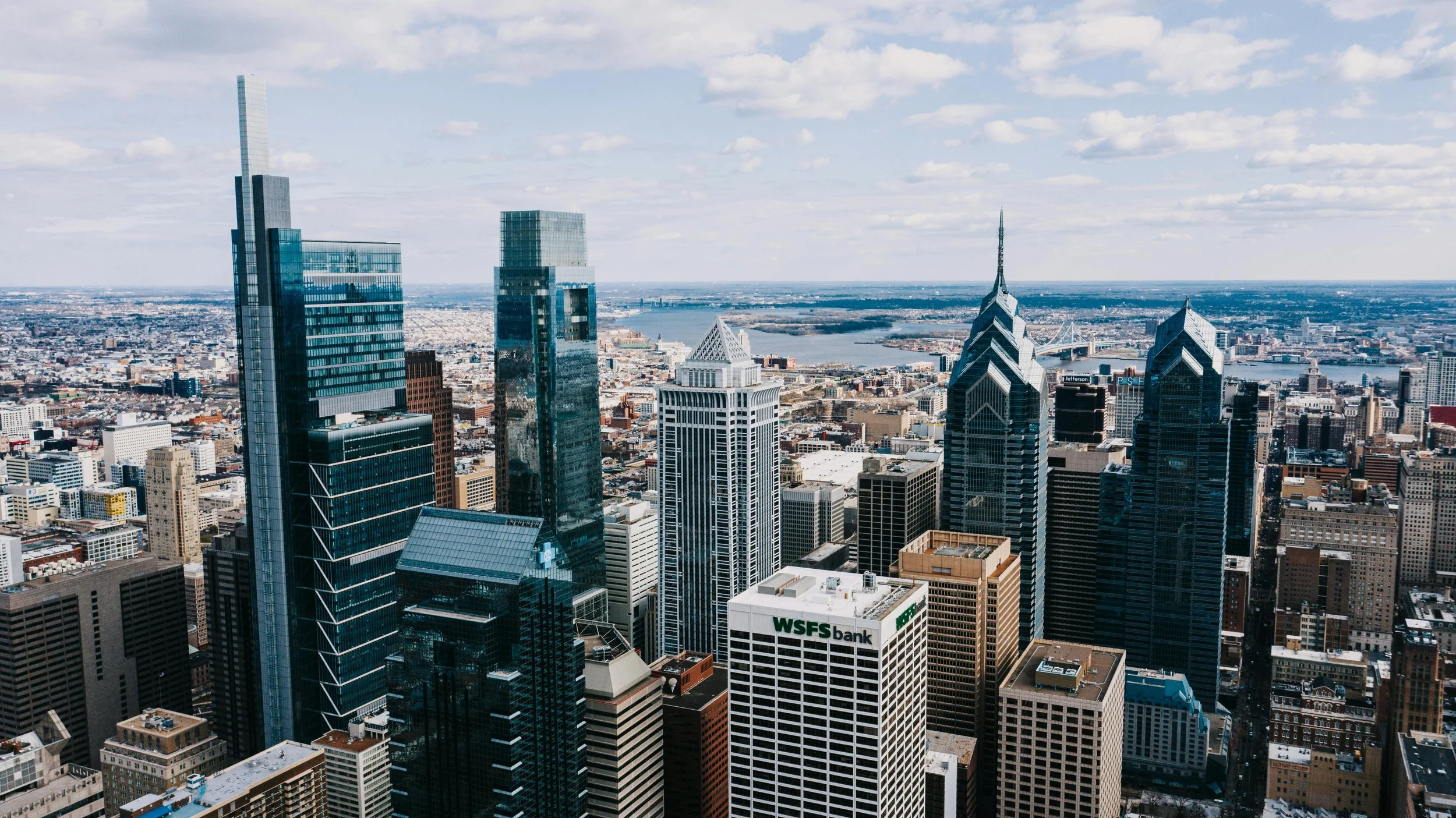 Aerial view of downtown Philadelphia skyline with skyscrapers and the Schuylkill River in the background.