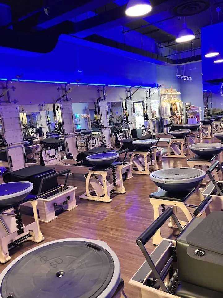 A row of Pilates reformer machines in a gym with blue lighting.