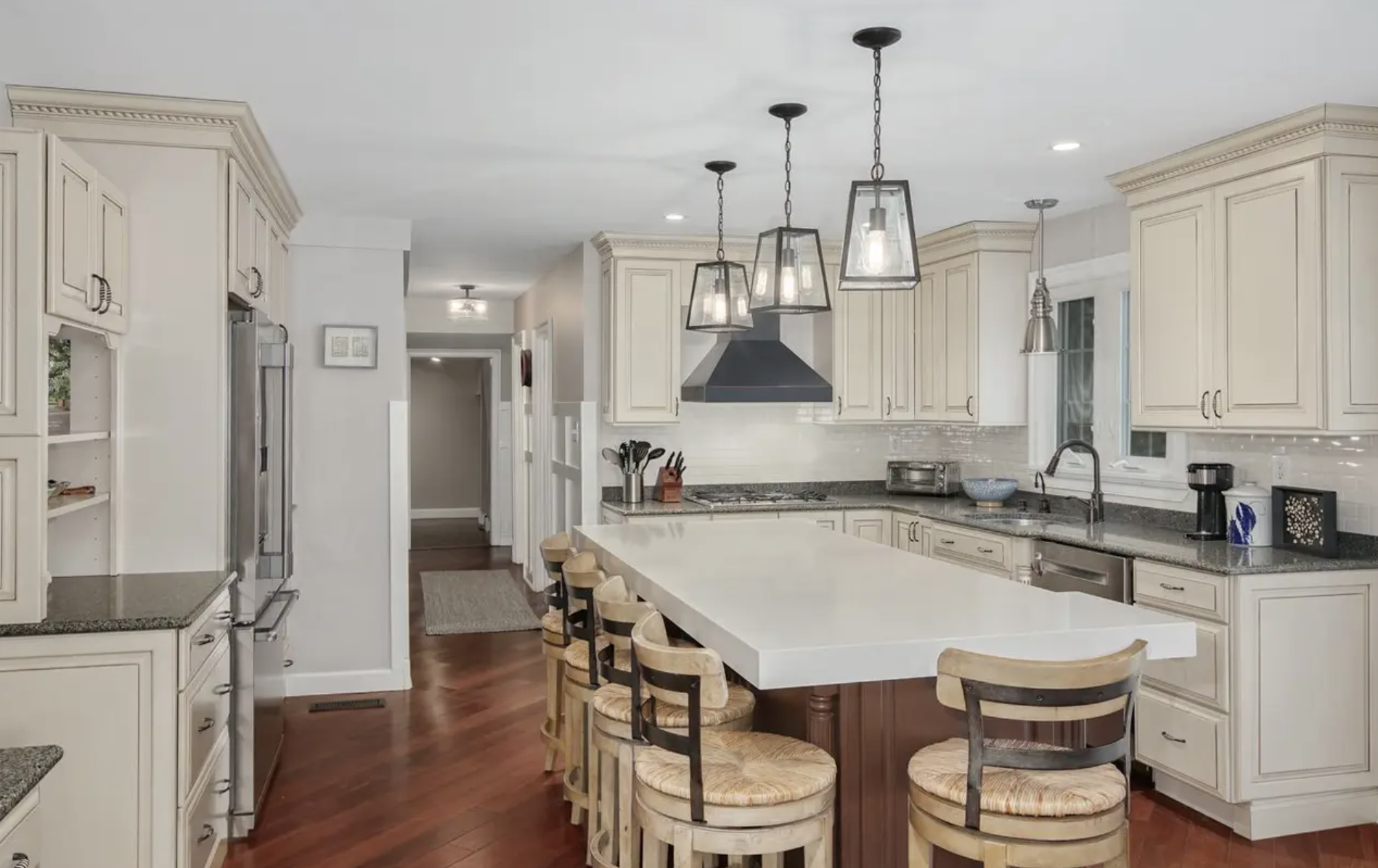 Bright kitchen with white cabinets, a large white island, hardwood floors, and modern pendant lights.