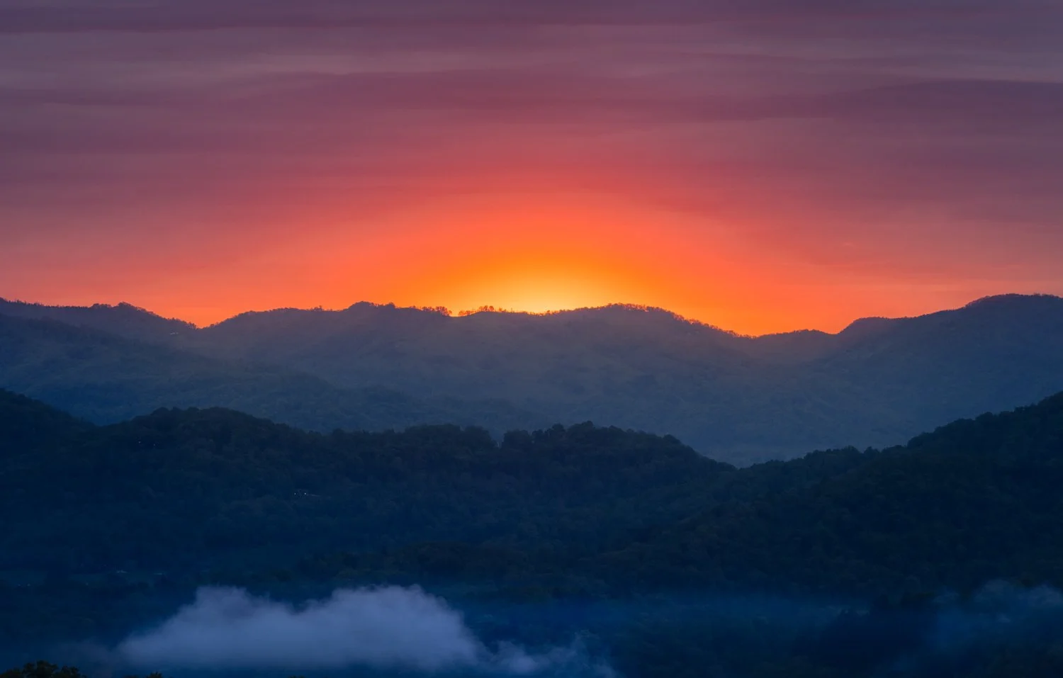 Sunset over mountain range with colorful sky and mist in the valleys.  This is the view from my front balcony in Waynesville, North Carolina.  The mountains are part of the Great Smokey Mountains