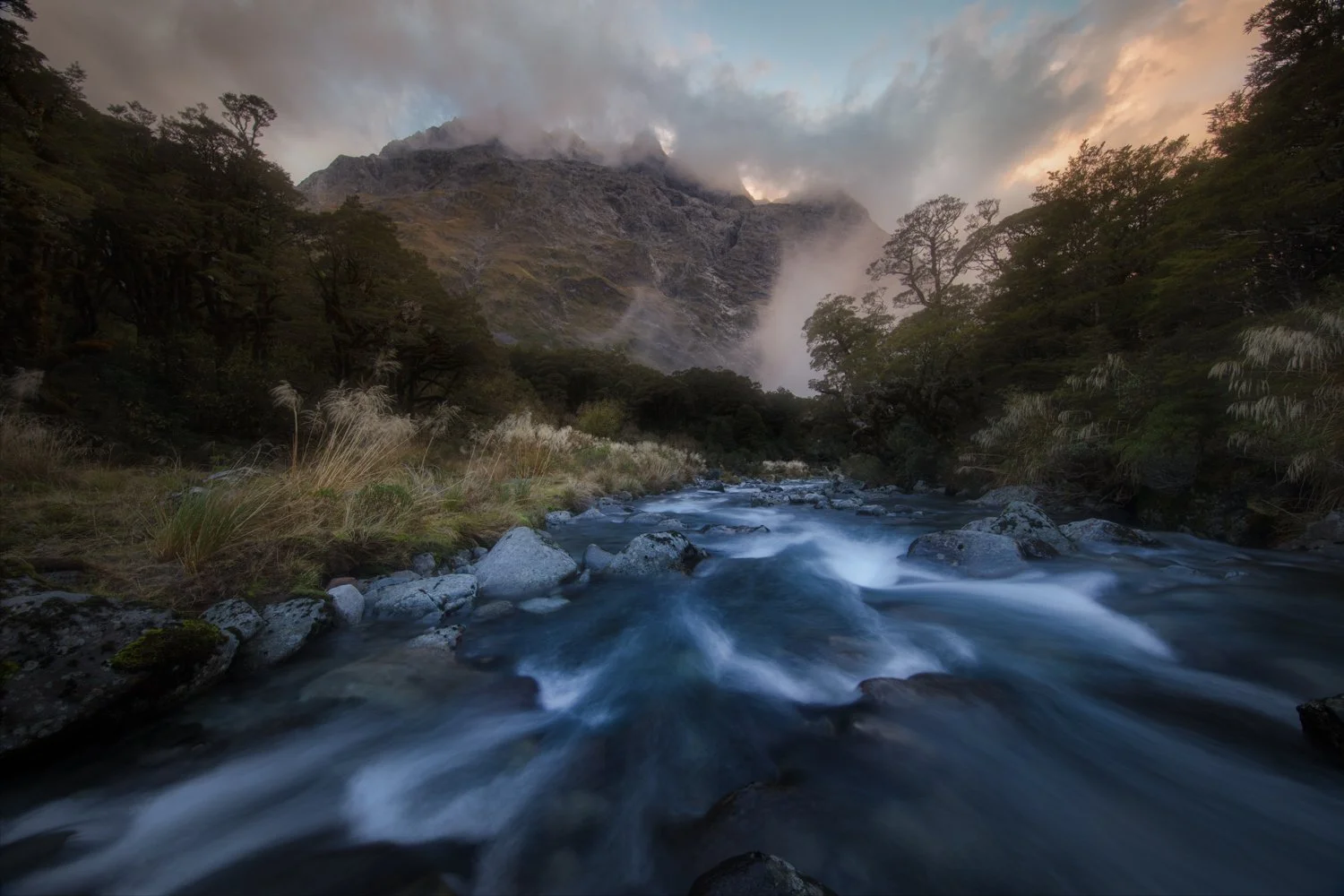 This was the first place we stopped at to shoot after we arrived at the South Island. It was a short hike after we parked the cars and noted a fast-moving river flows through a lush green forest in New Zealand, with tall trees on both sides and mist 