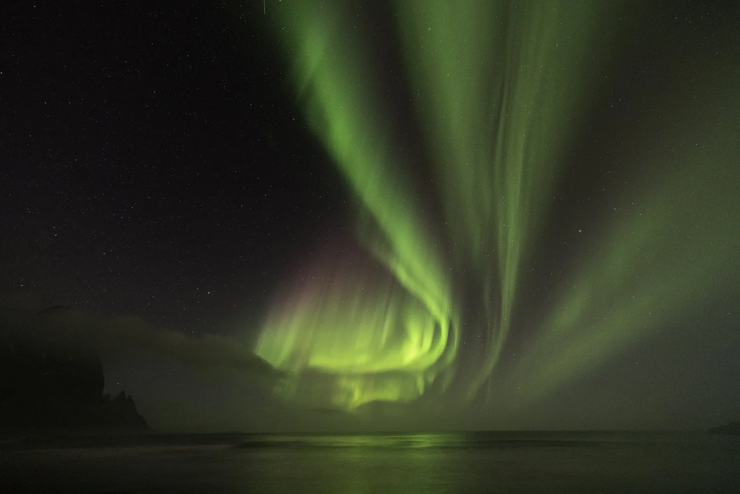 Northern lights (aurora borealis) in Iceland over the ocean at night with a starry sky.