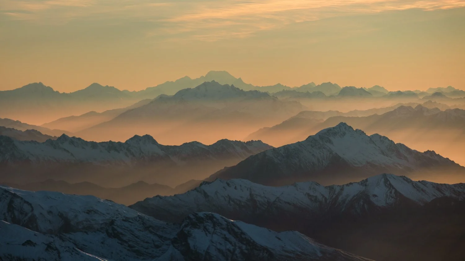 Sunrise over snow-capped mountain ranges with layers of peaks fading into the distance. The tallest peak in the last layer is Mount Cook in New Zealand.  I took this shot via helicopter.