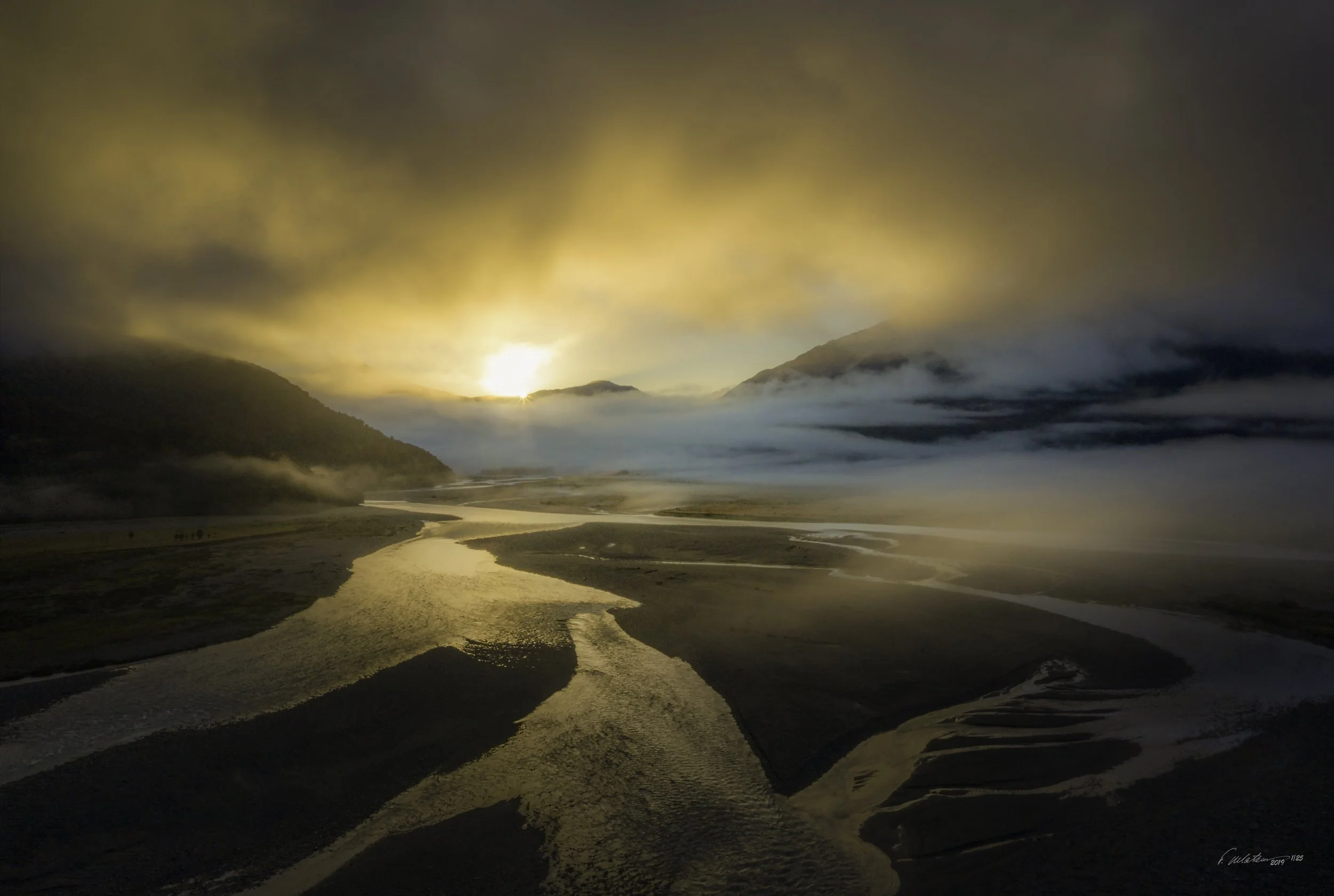 Sunset over a river valley with mountains and clouds.  Shot taken by drone