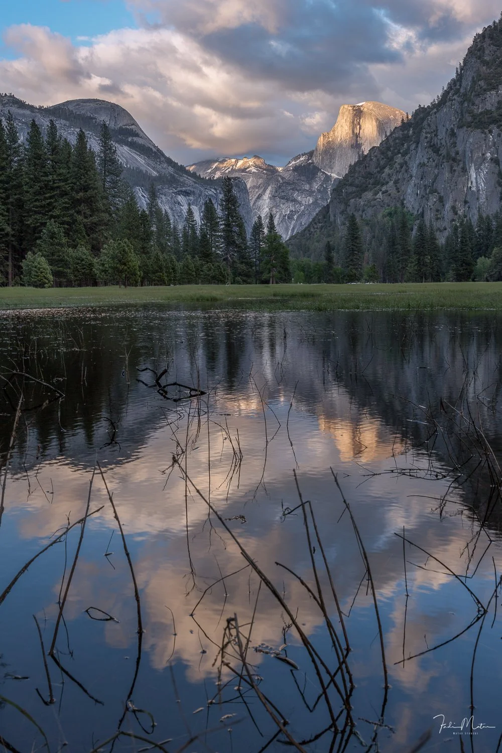 Scenic view of a mountain landscape with reflections in a lake, pine trees, and a partly cloudy sky