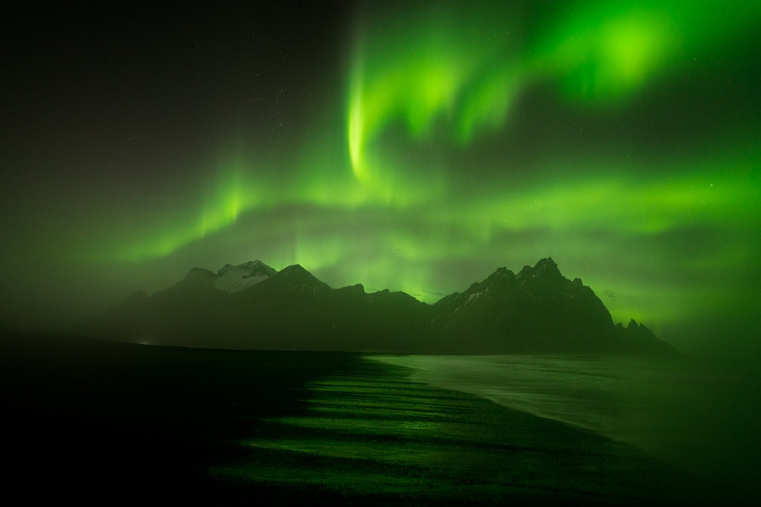 Green Northern Lights over a mountainous landscape at night.
