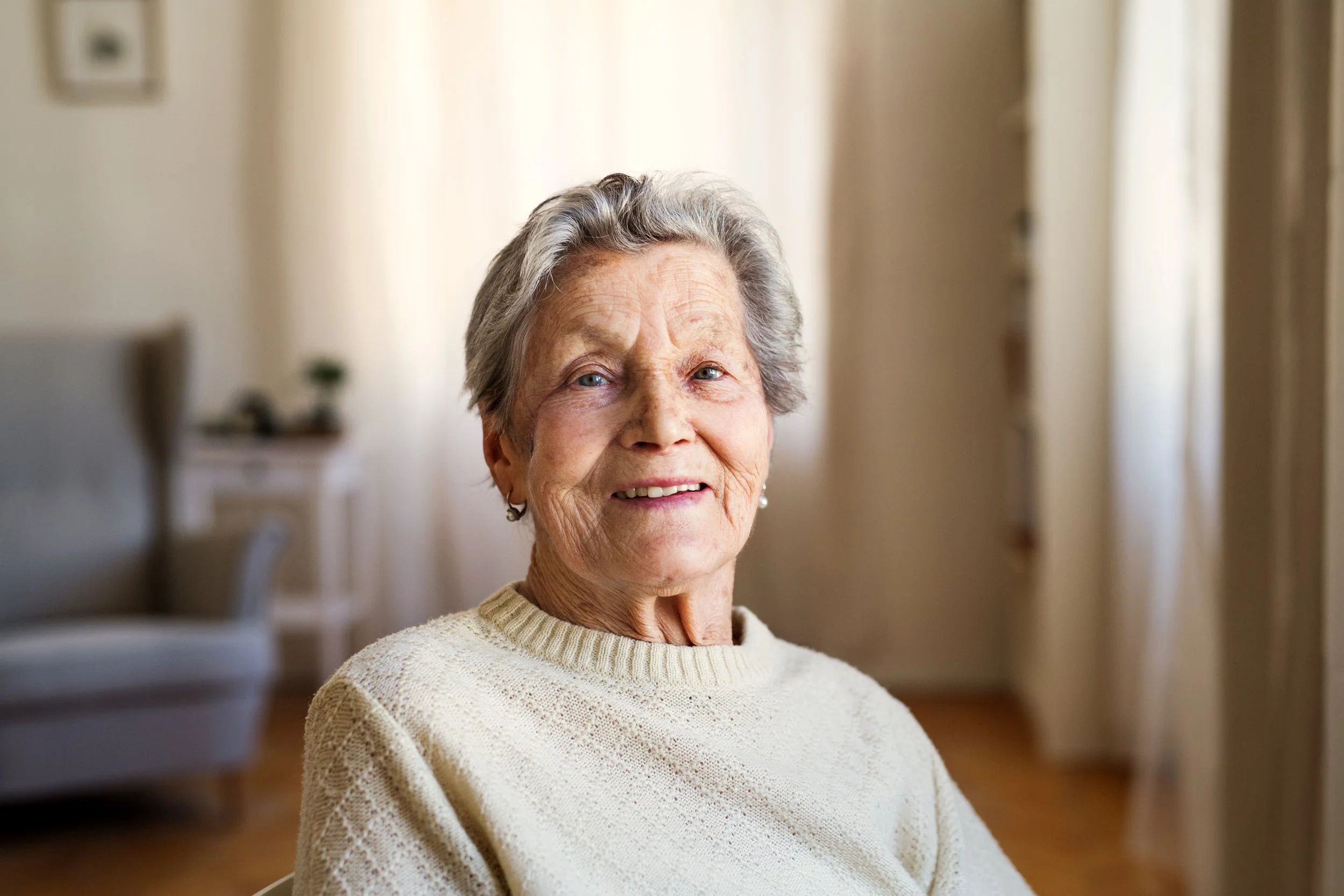 Senior woman with gray hair smiling indoors in a cozy room.